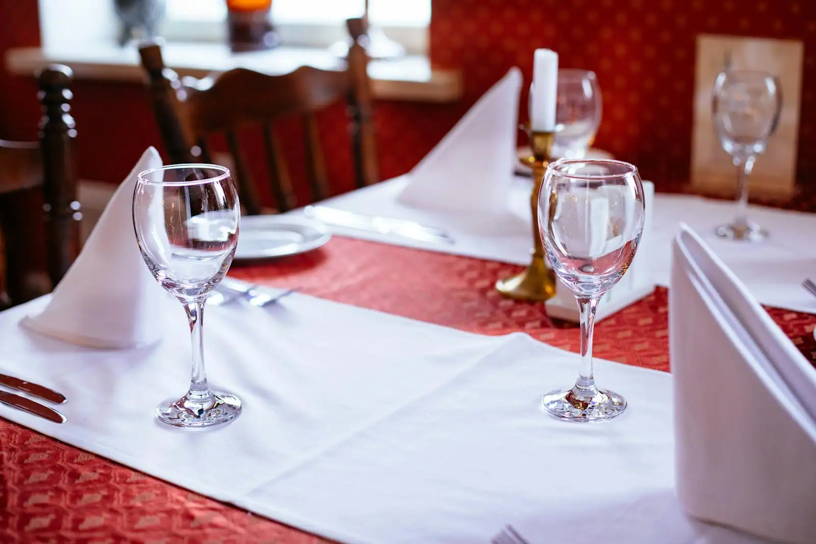 Table dressée avec un verre de vin rouge à demi rempli, assiette dans le flou en arrière-plan, ambiance restaurant tamisée