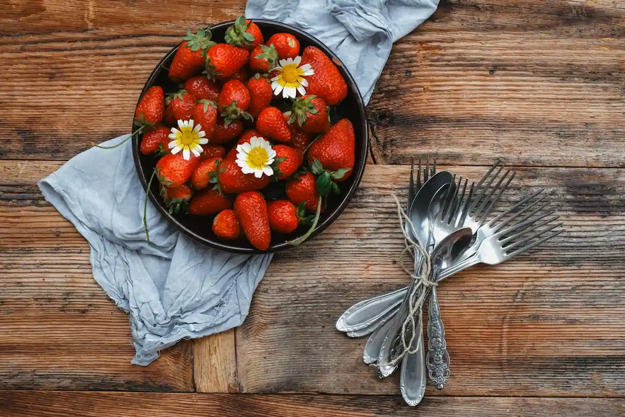 Fraises fraîches dans un panier en bois sur une table de cuisine, sucre et basilic à côté