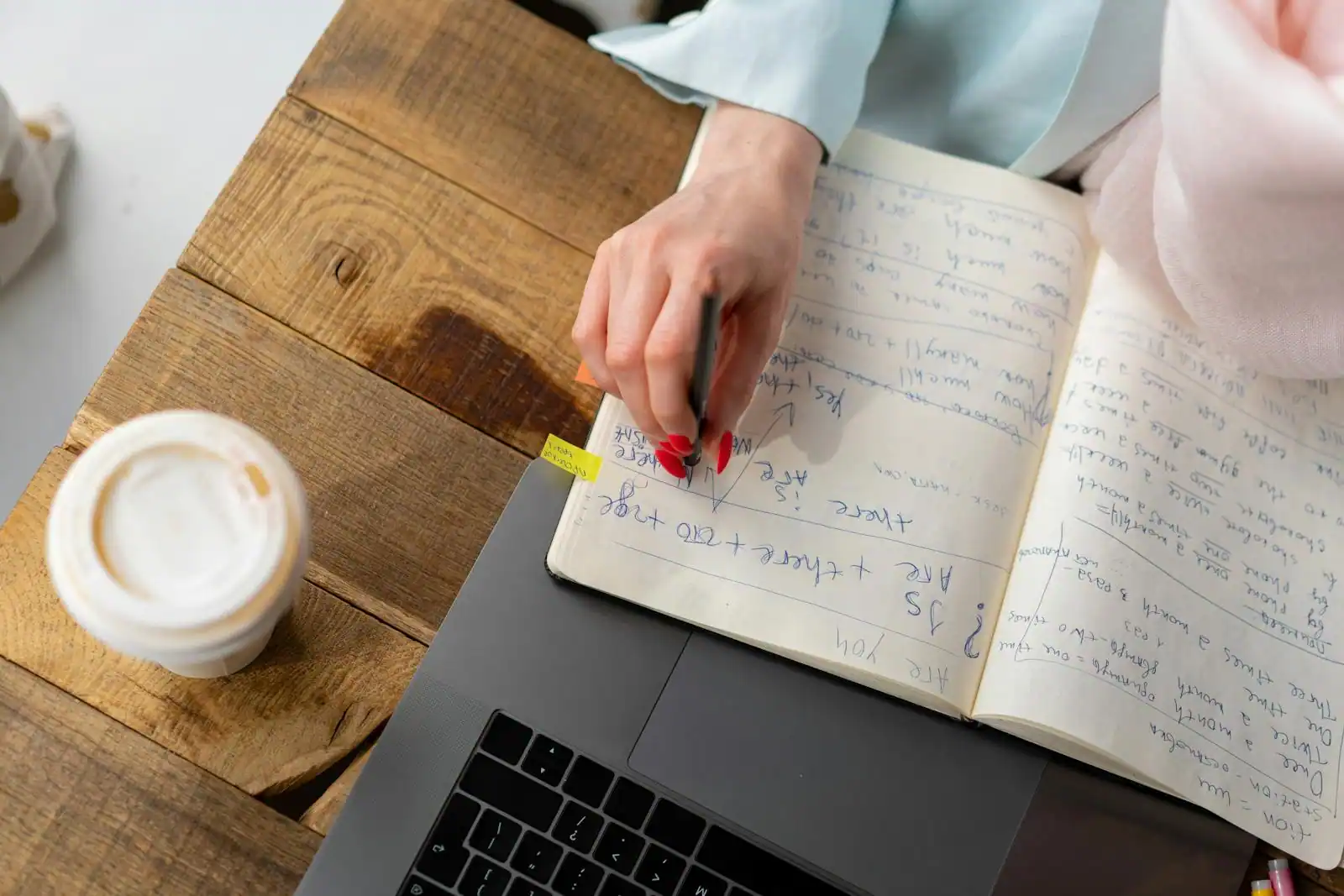 Livres de cuisine empilés sur une table en bois, à côté d'une tasse de café et de notes manuscrites