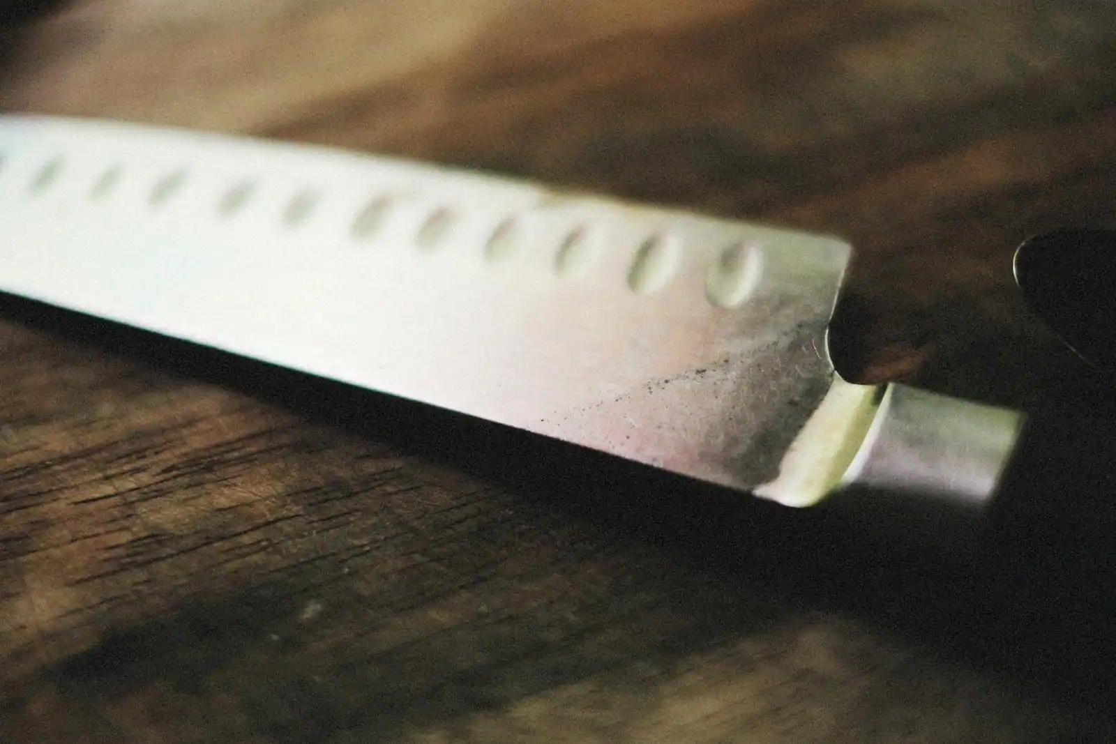 Couteau de chef en acier, sauteuse en inox et poêle en fer noir disposés sur un plan de travail en bois