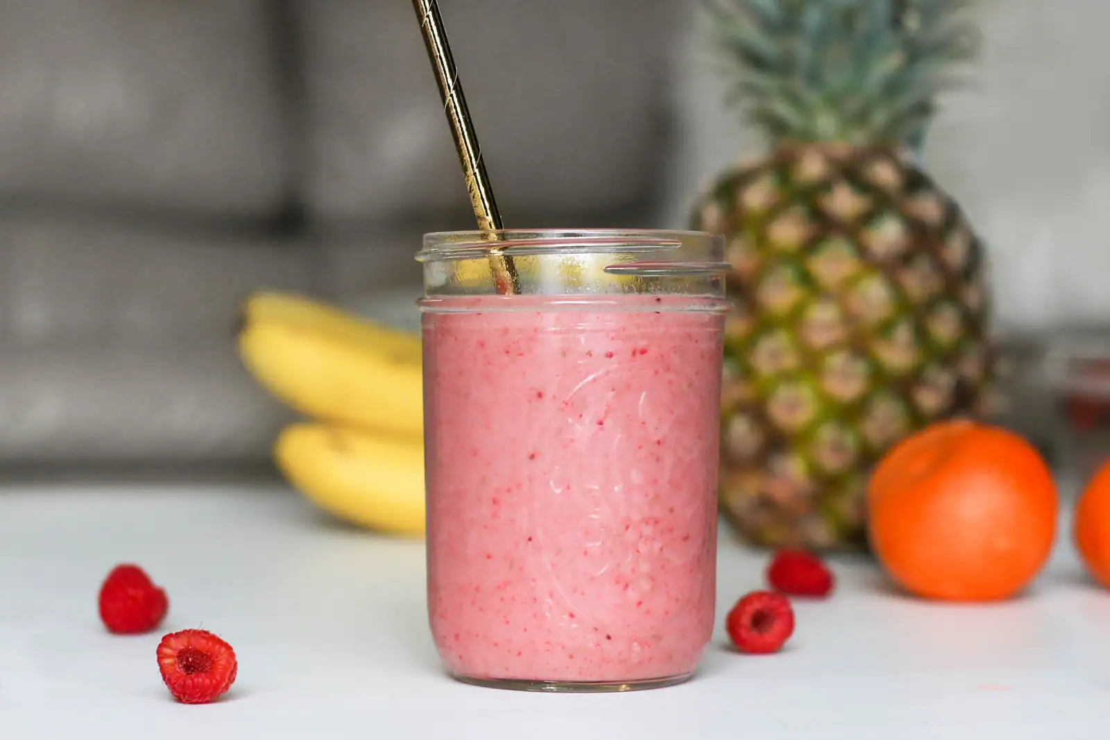 Un smoothie maison dans un bocal en verre avec une paille, entouré de banane et de fruits frais.