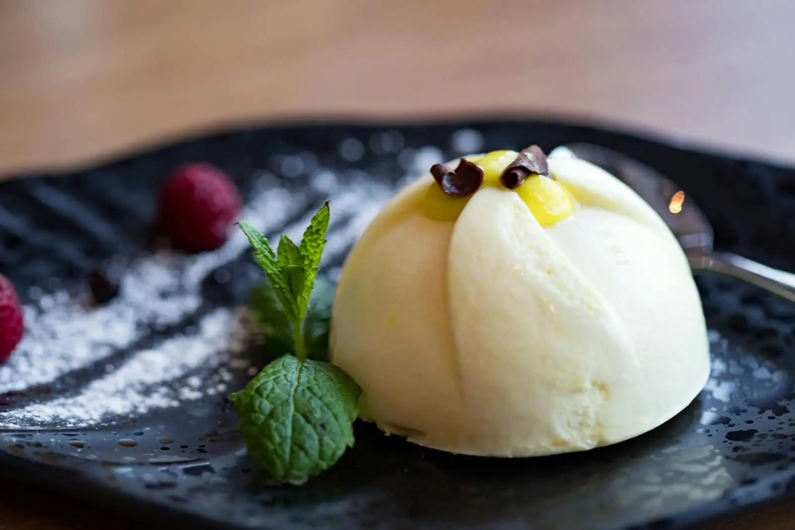 Dessert crémeux en dôme accompagné de framboises fraîches et de menthe sur une assiette