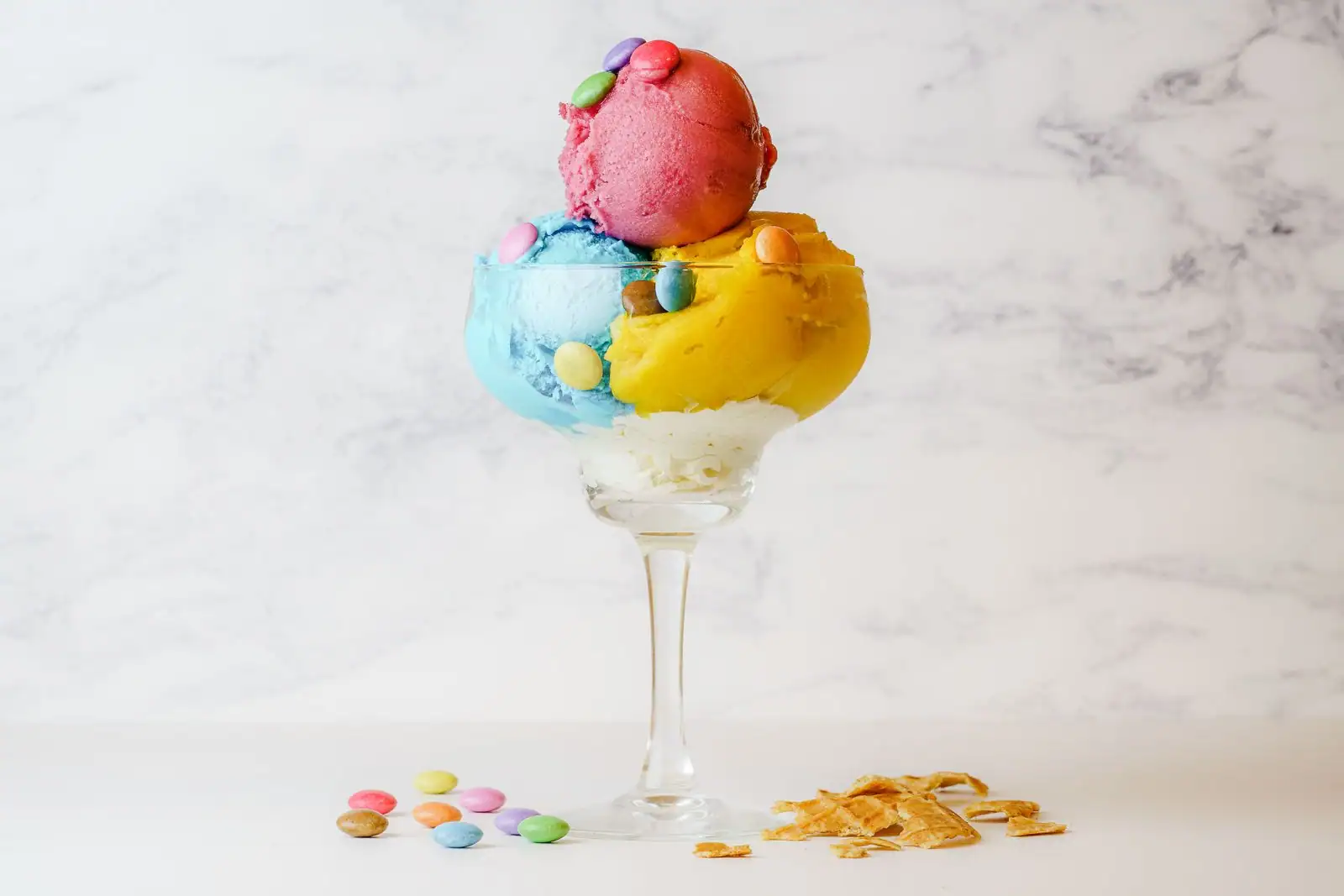 Boules de glace colorées garnies de bonbons, servies dans une coupe sur fond clair.