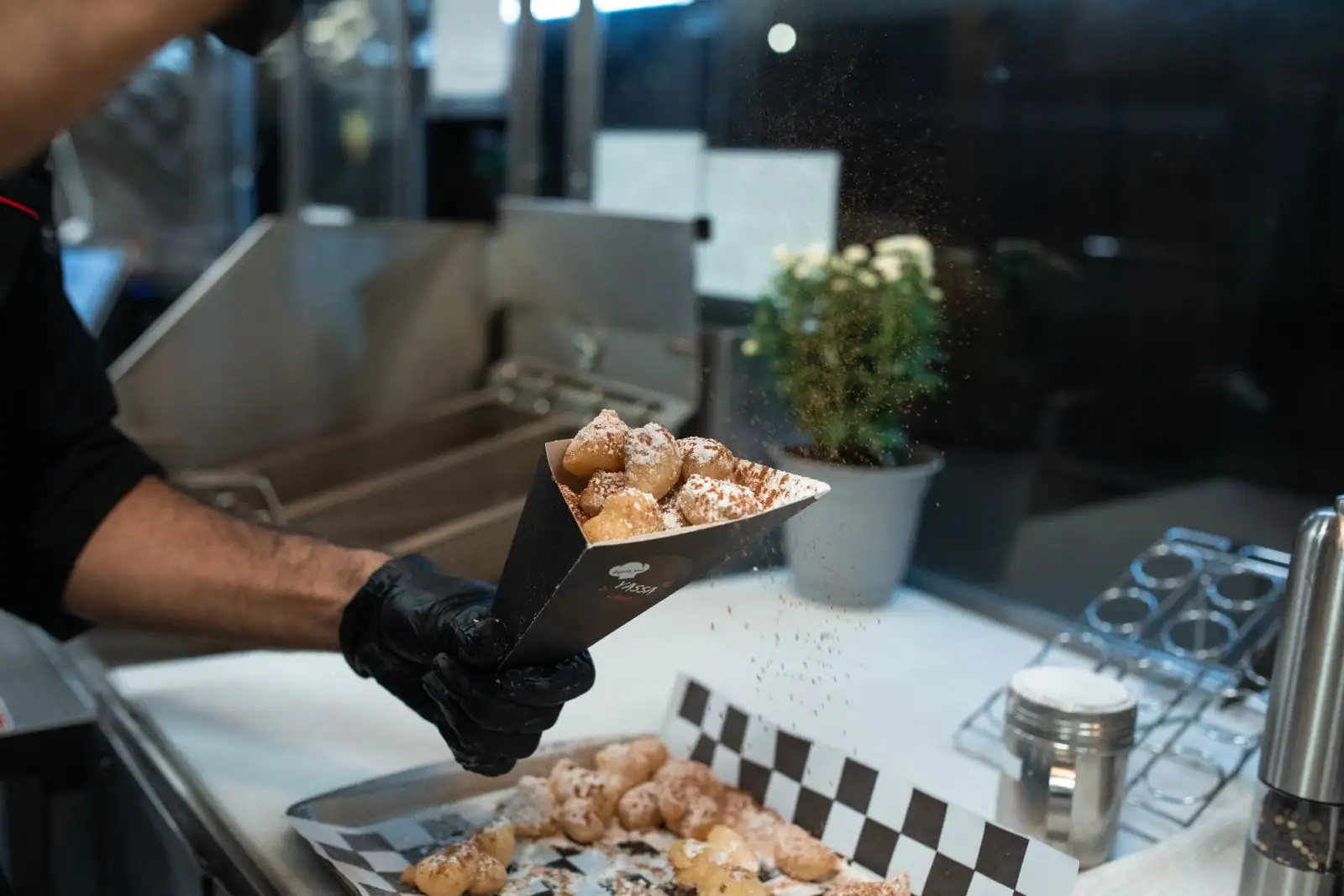 Beignets frits saupoudrés de sucre glace, servis dans un cornet de papier sur un stand gourmand.