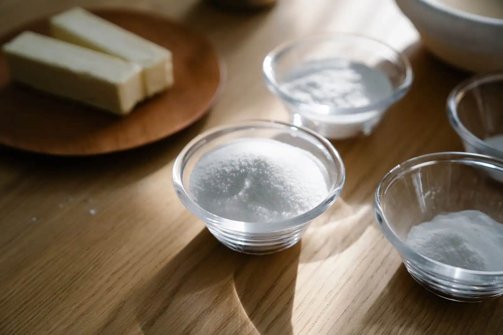Bols en verre contenant de la farine, du sucre et du beurre sur un plan de travail en bois, pour la pâtisserie.