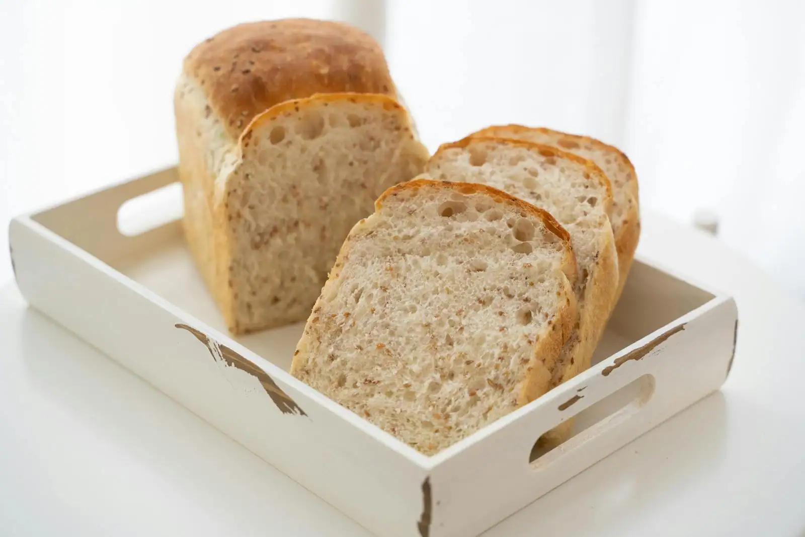 Pain maison tranché présenté dans un plateau en bois blanc