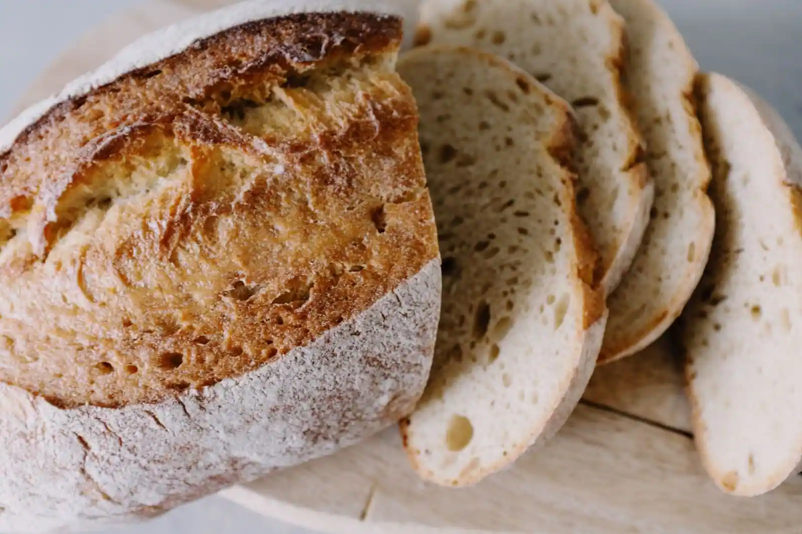 Pain rustique à la croûte farinée, tranché en plusieurs morceaux sur une planche en bois, mie aérée visible