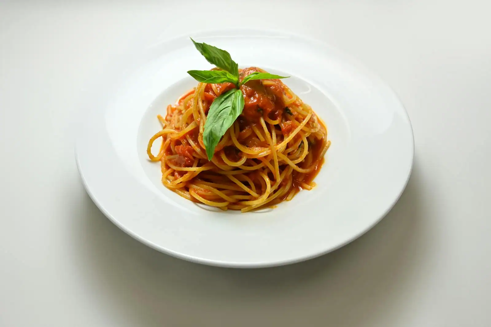 Assiette de spaghetti nappés de sauce tomate, garnis d'une feuille de basilic