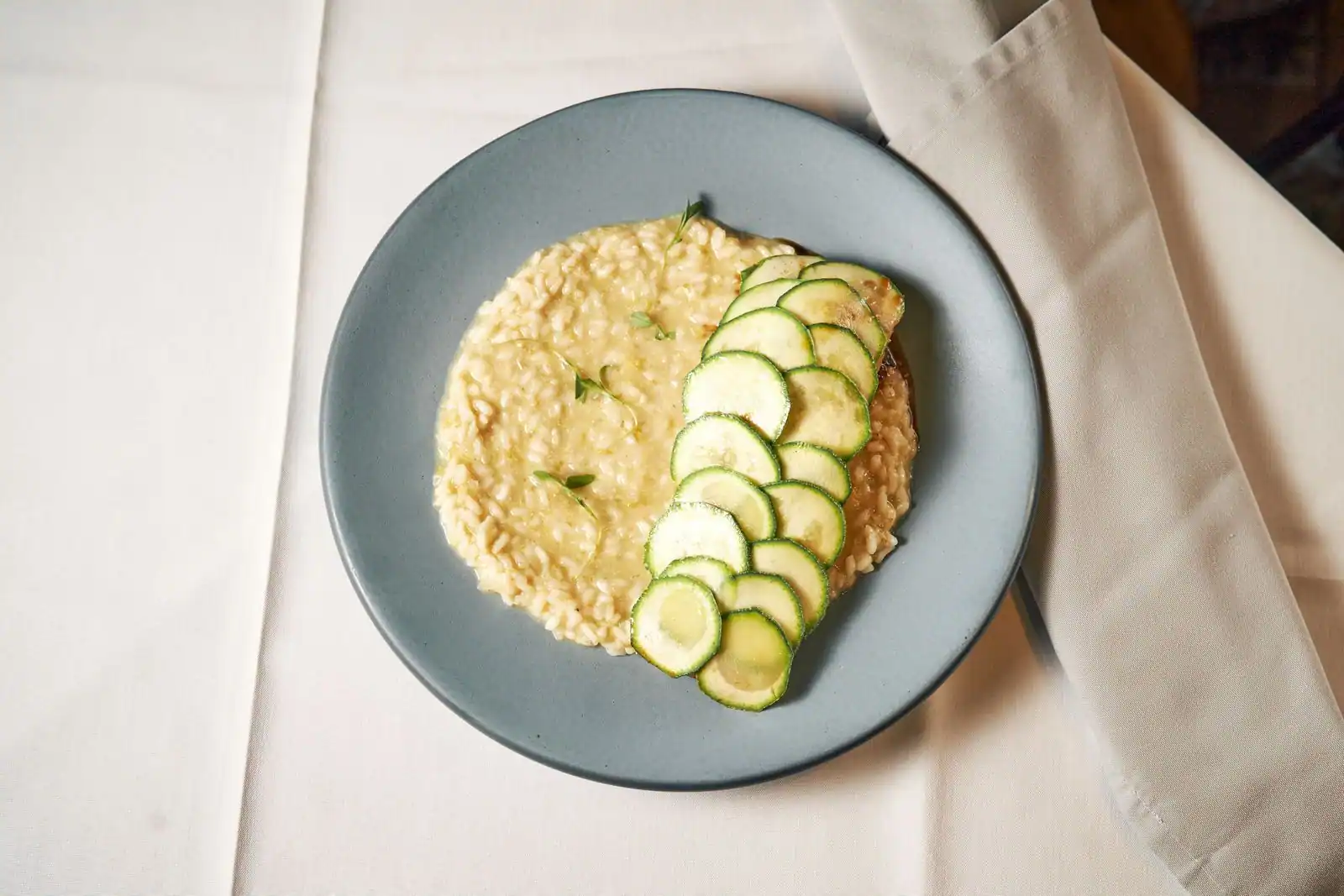 Assiette de risotto crémeux garni de fines tranches de courgette, riz nacré et onctueux.