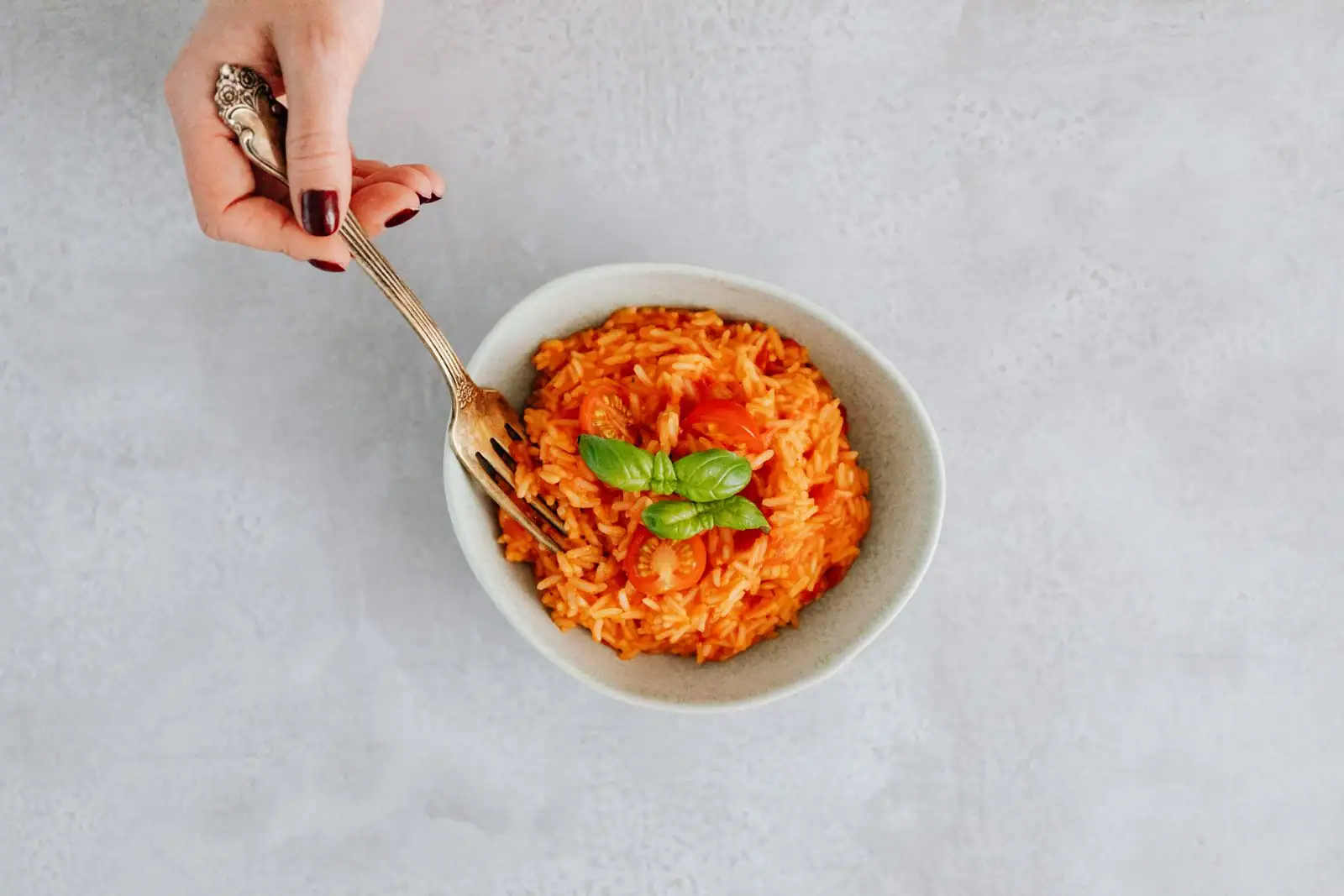 Bol de risotto à la tomate, garni de tomates cerises et de feuilles de basilic frais.