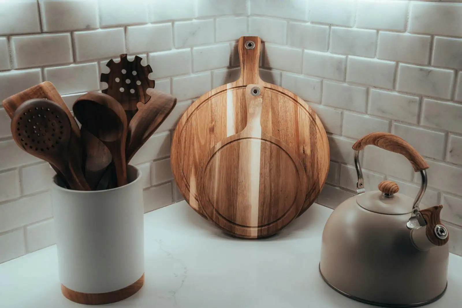 Ustensiles de cuisine en bois dans un pot et planche à découper ronde sur un plan de travail clair