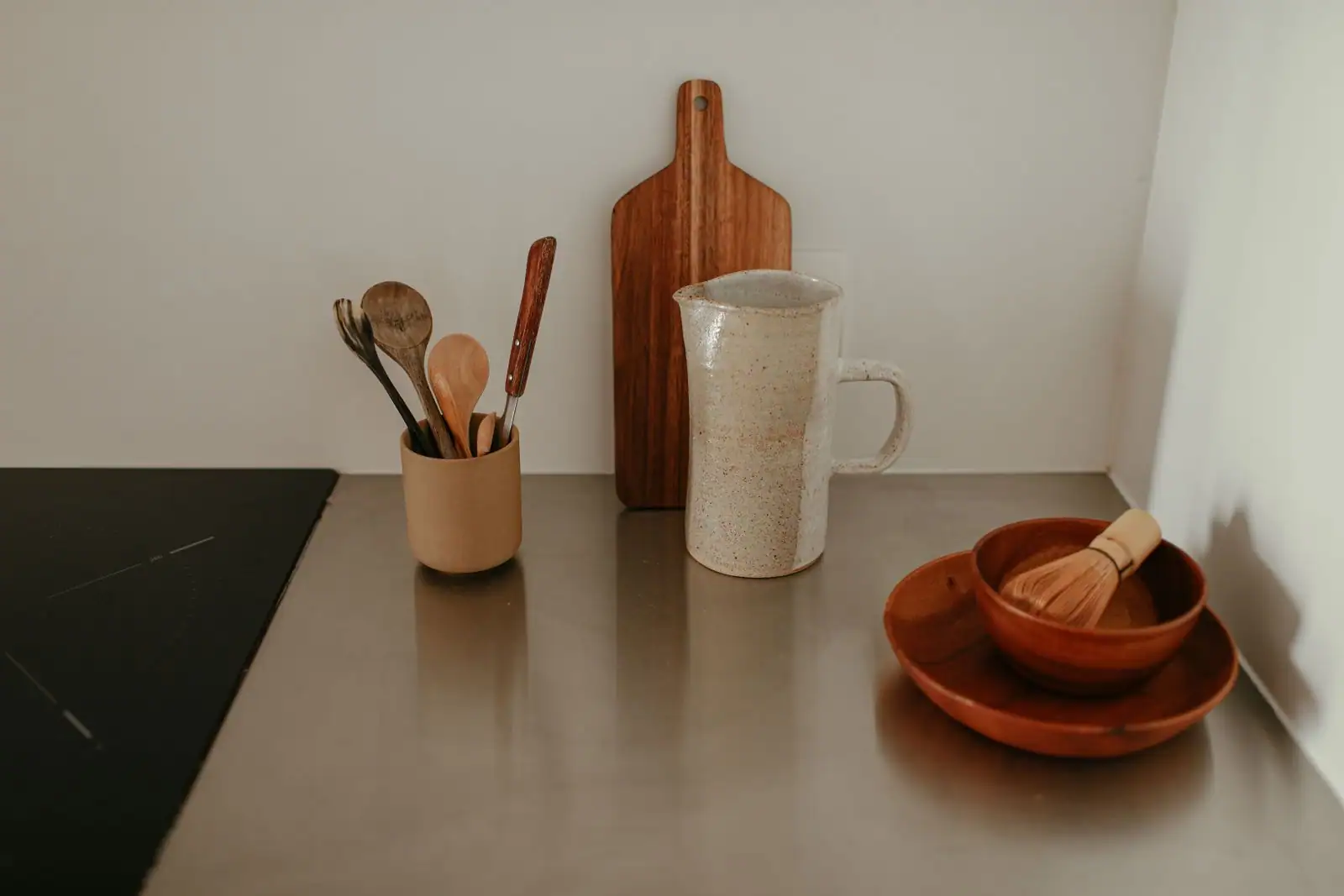 Ustensiles de cuisine en bois dans un pot, planche à découper et bol posés sur un plan de travail.