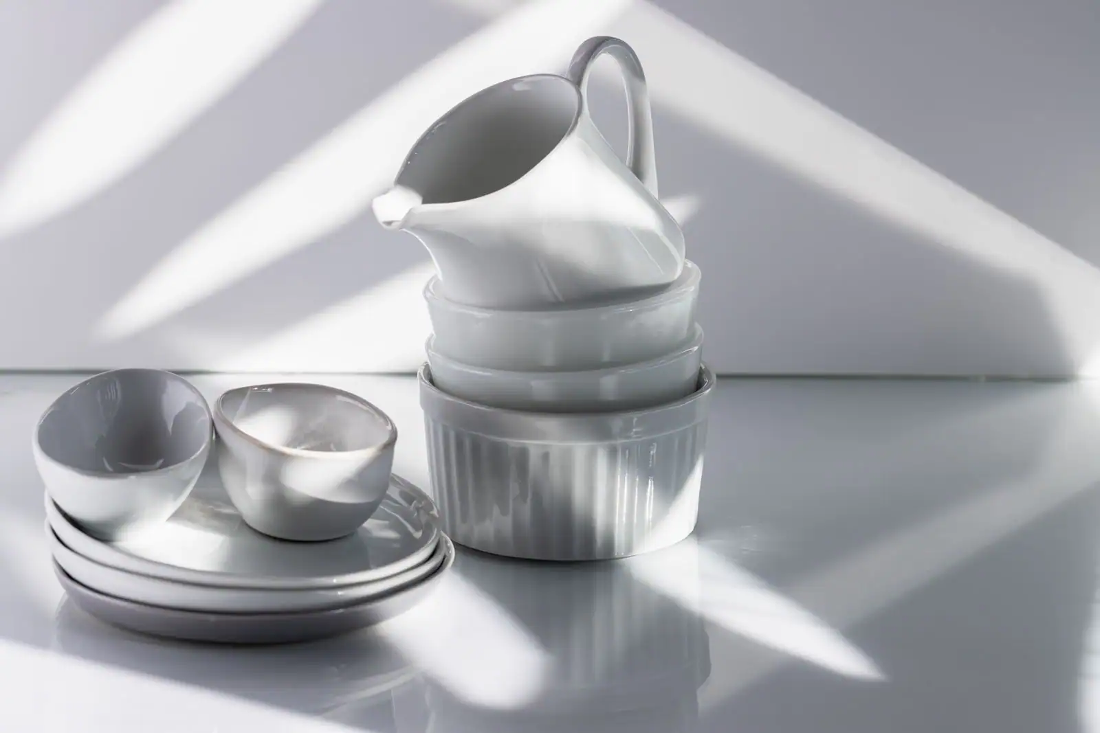 Un ensemble de vaisselle blanche en porcelaine — assiettes, bols et pichet — disposé sous une lumière de studio.