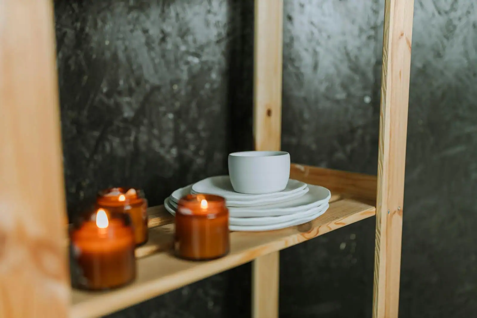 Assiettes et bol en céramique blanche empilés sur une étagère en bois, à côté de bougies allumées