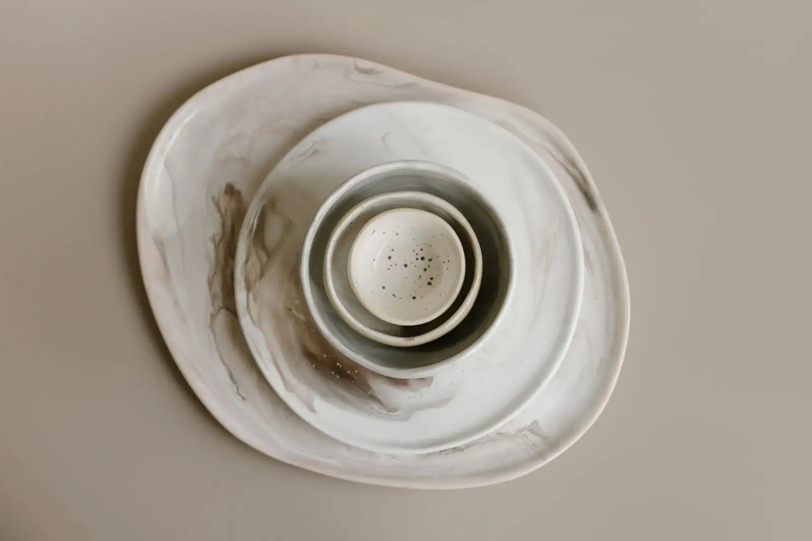 Vaisselle en céramique aux tons neutres : assiettes et bols imbriqués, vus de dessus.
