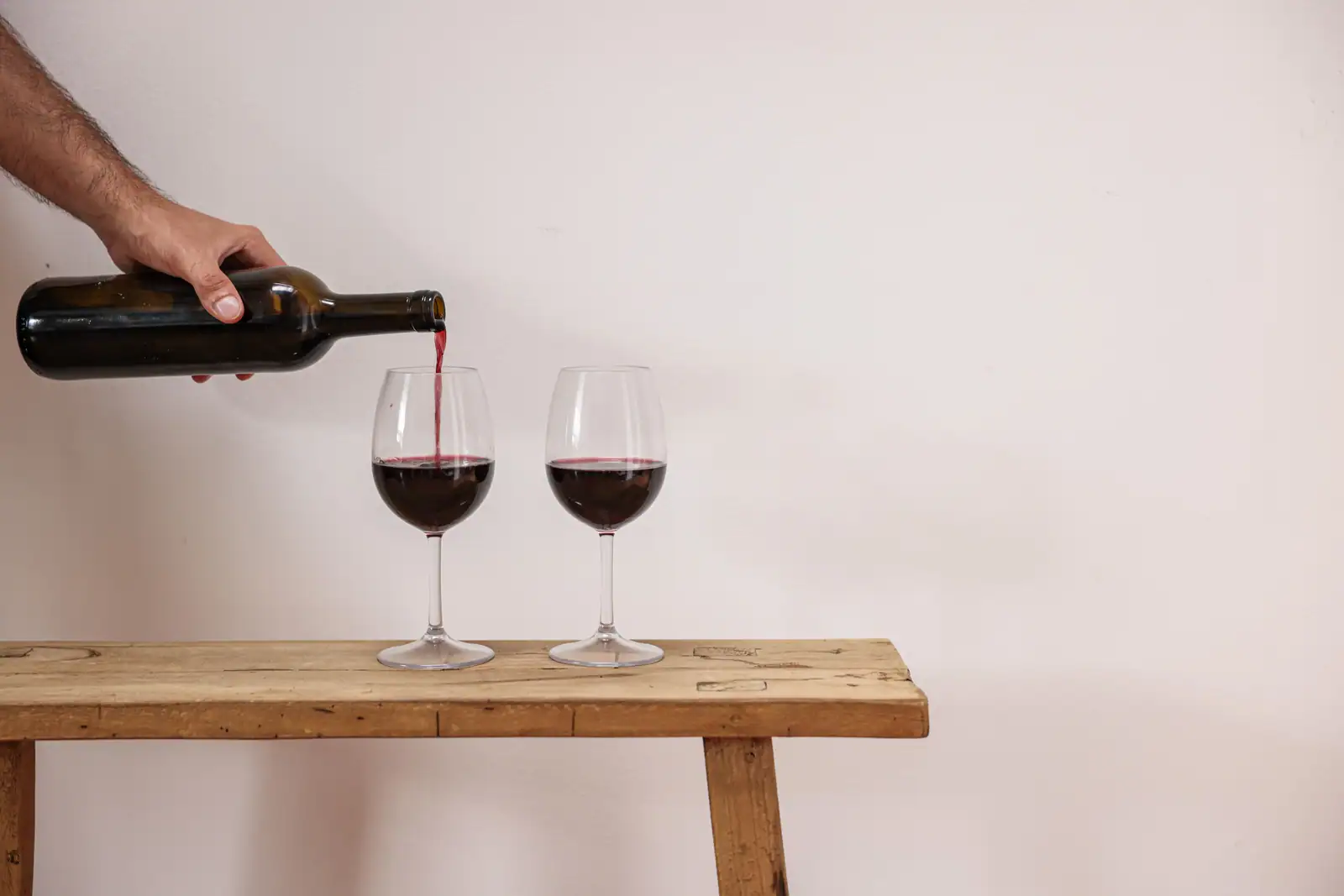 Vin rouge versé d'une bouteille dans deux verres, posés sur une table en bois rustique.