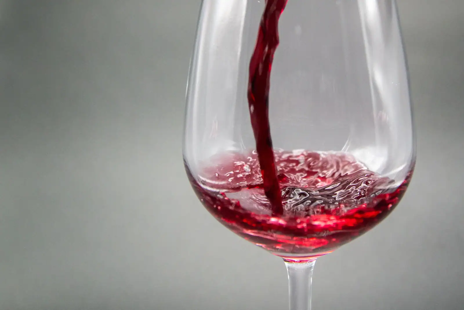 Vin rouge versé dans un verre à pied, photographié en gros plan sur un fond gris neutre.