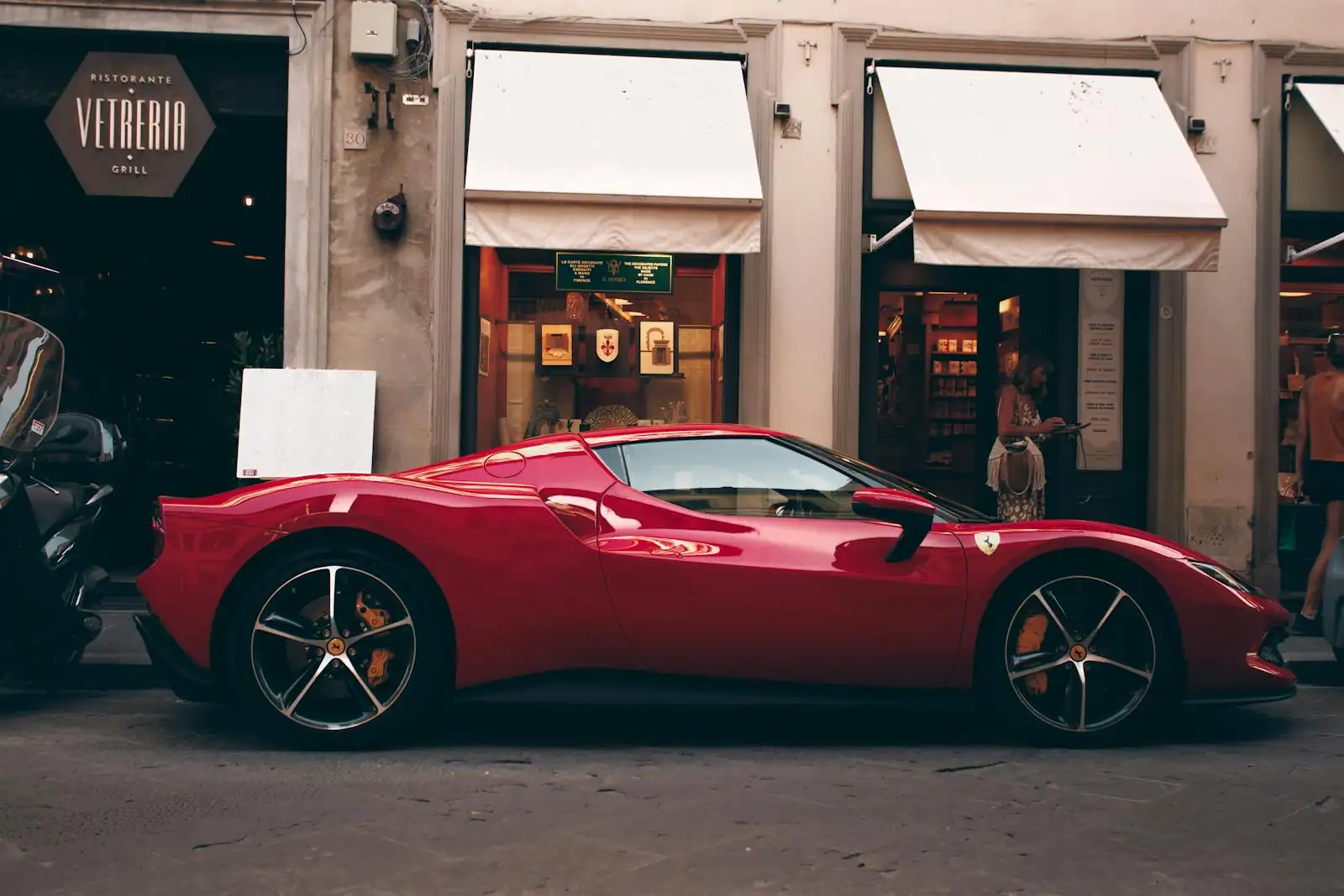 Voiture de sport italienne rouge, de profil, garée dans une rue commerçante ensoleillée