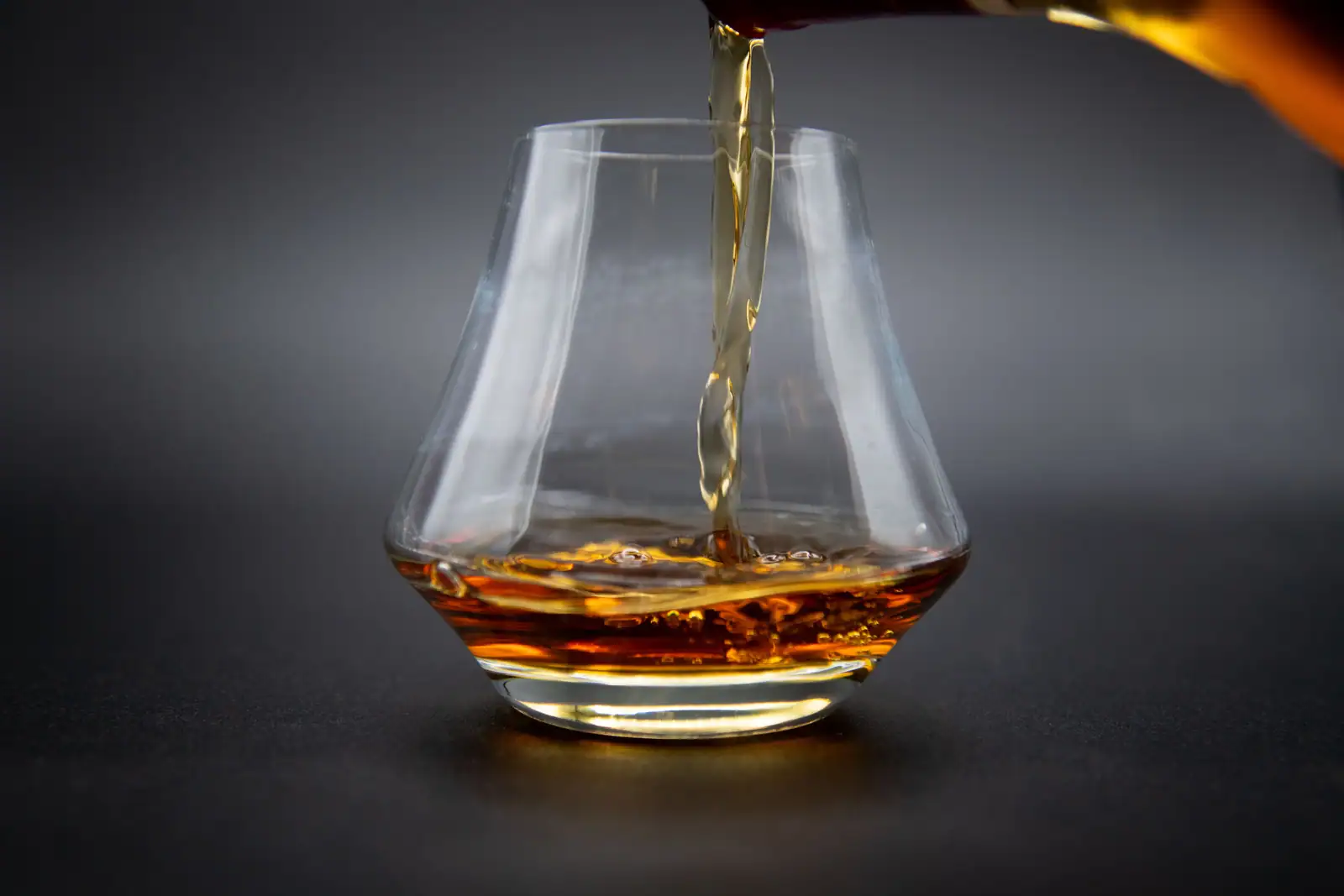 Whisky ambré versé dans un verre tulipe de dégustation, sur fond sombre.
