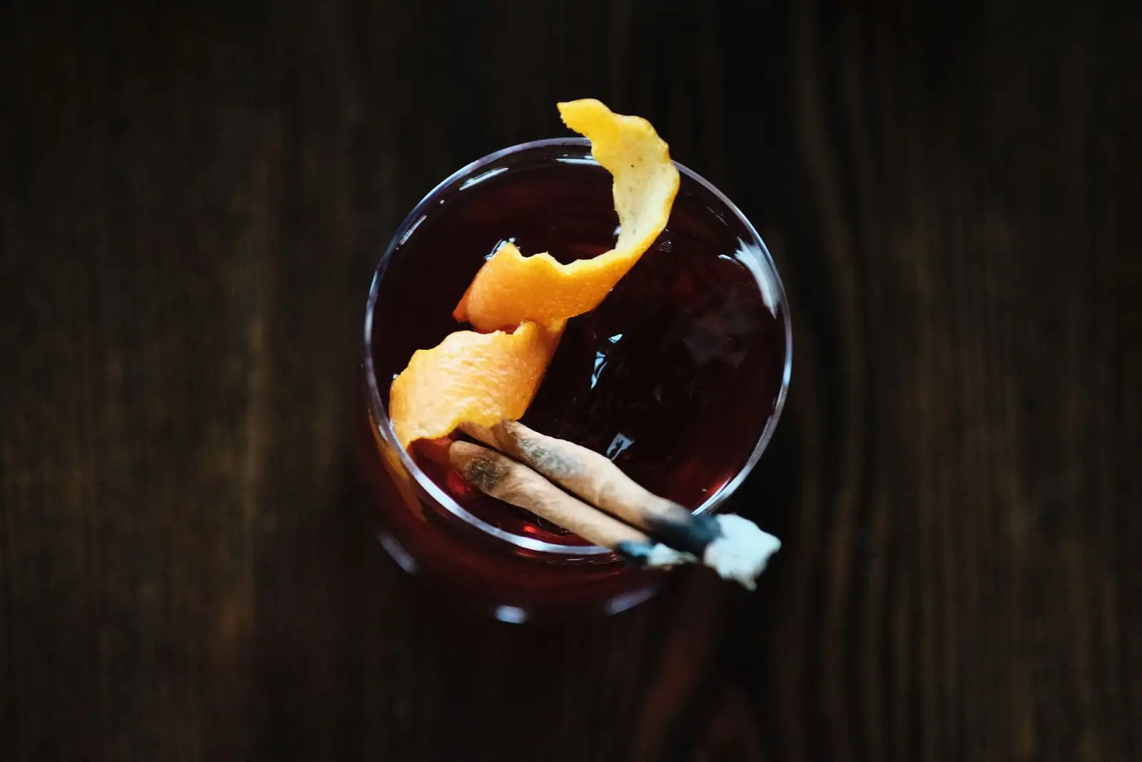 Cocktail negroni rouge orangé garni d'un long zeste d'orange, photographié de dessus