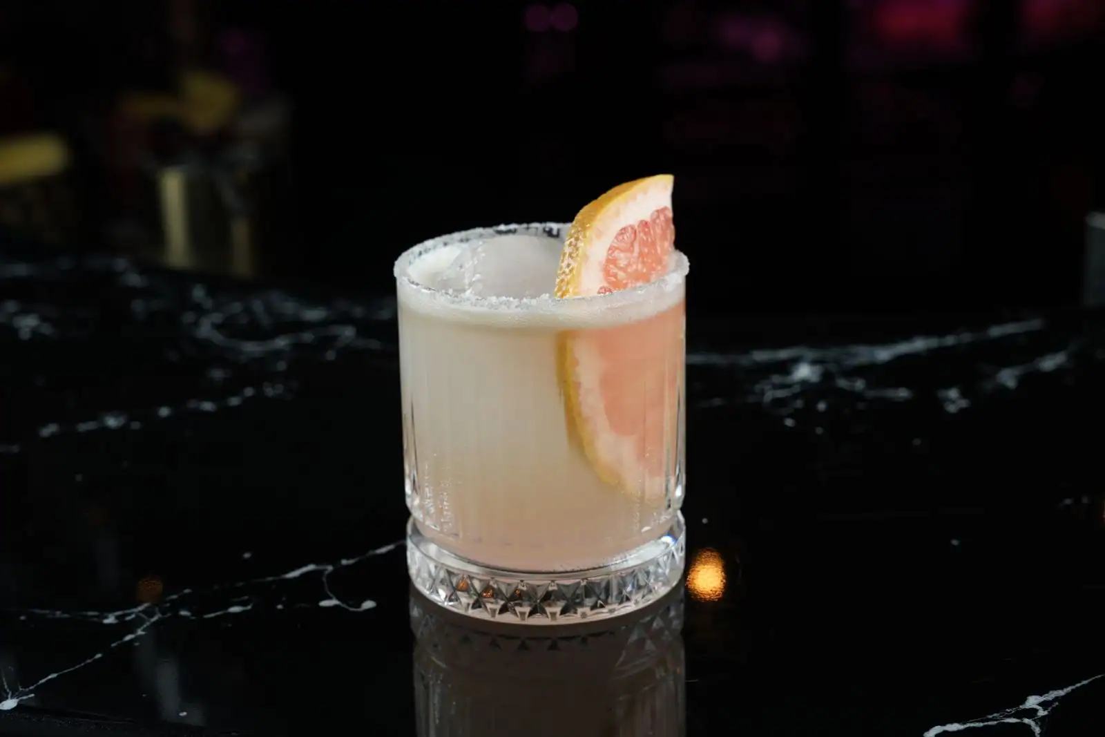 Cocktail Paloma au pamplemousse, bord du verre givré de sel et quartier de pamplemousse en garniture, sur fond sombre