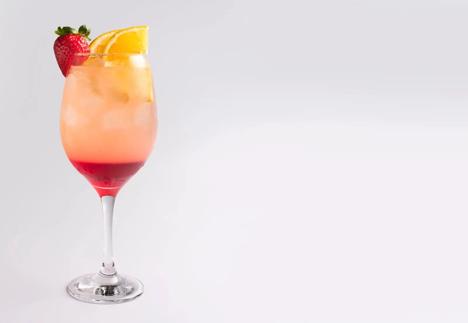 Cocktail au dégradé orange et rouge, garni d'une tranche d'orange et d'une fraise, servi sur glace
