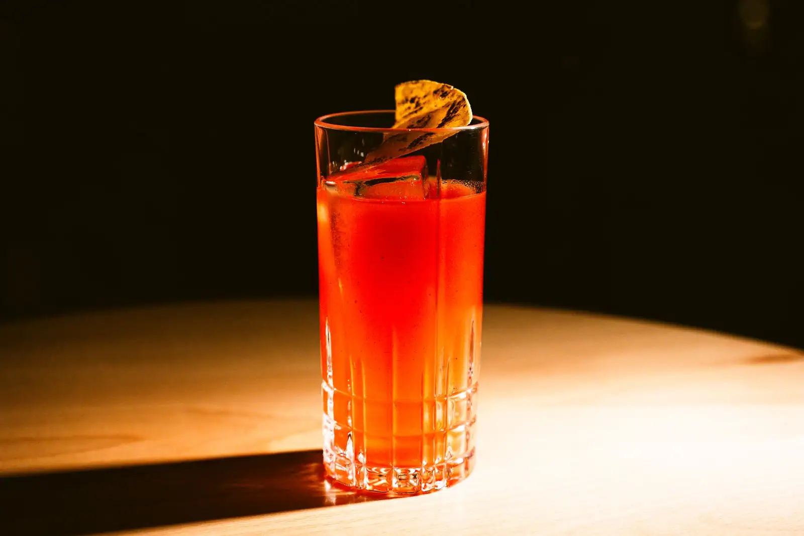 Cocktail orangé servi sur glace dans un grand verre, garni d'une tranche d'orange séchée