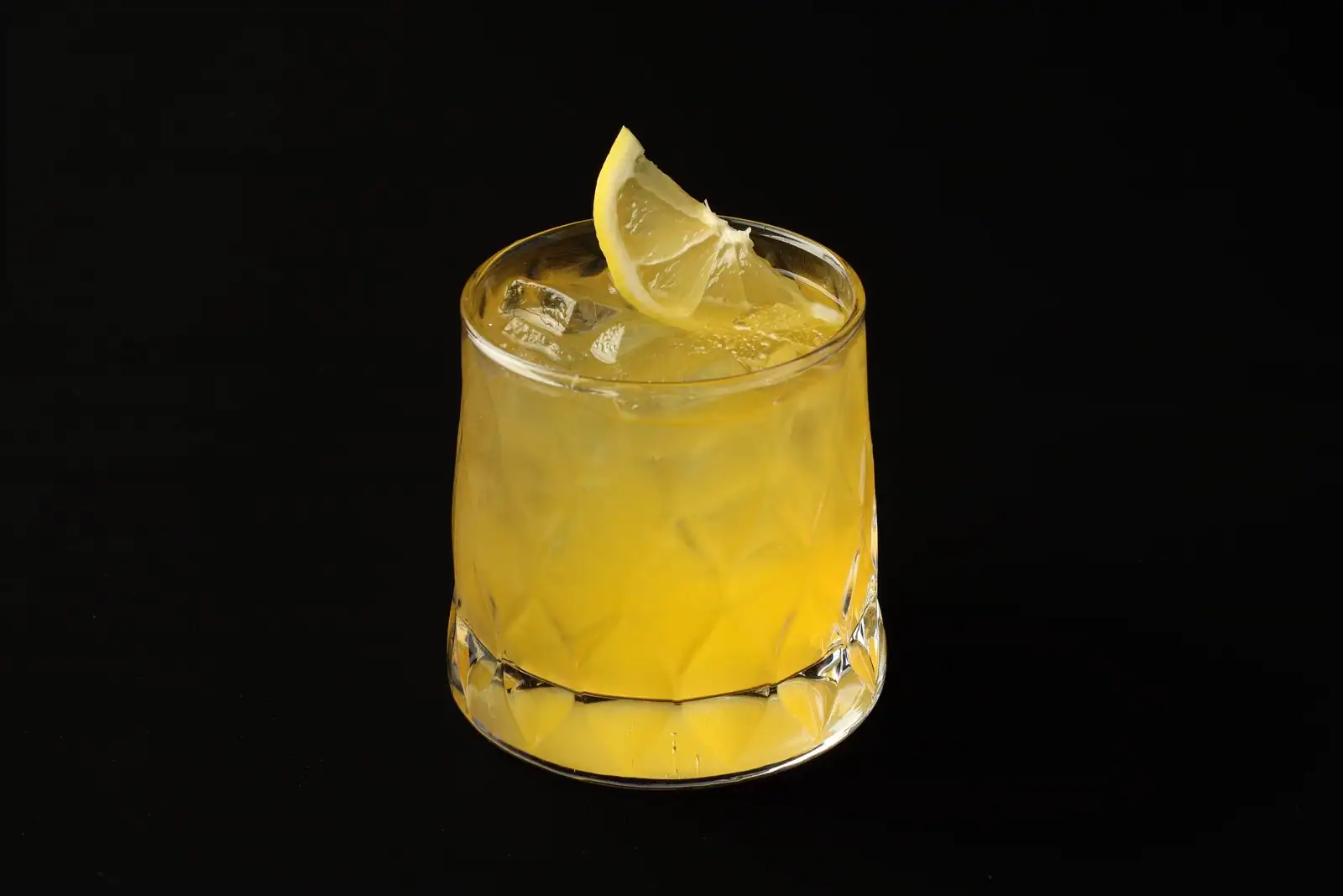 Cocktail jaune aux agrumes servi sur glace avec une tranche de citron dans un verre