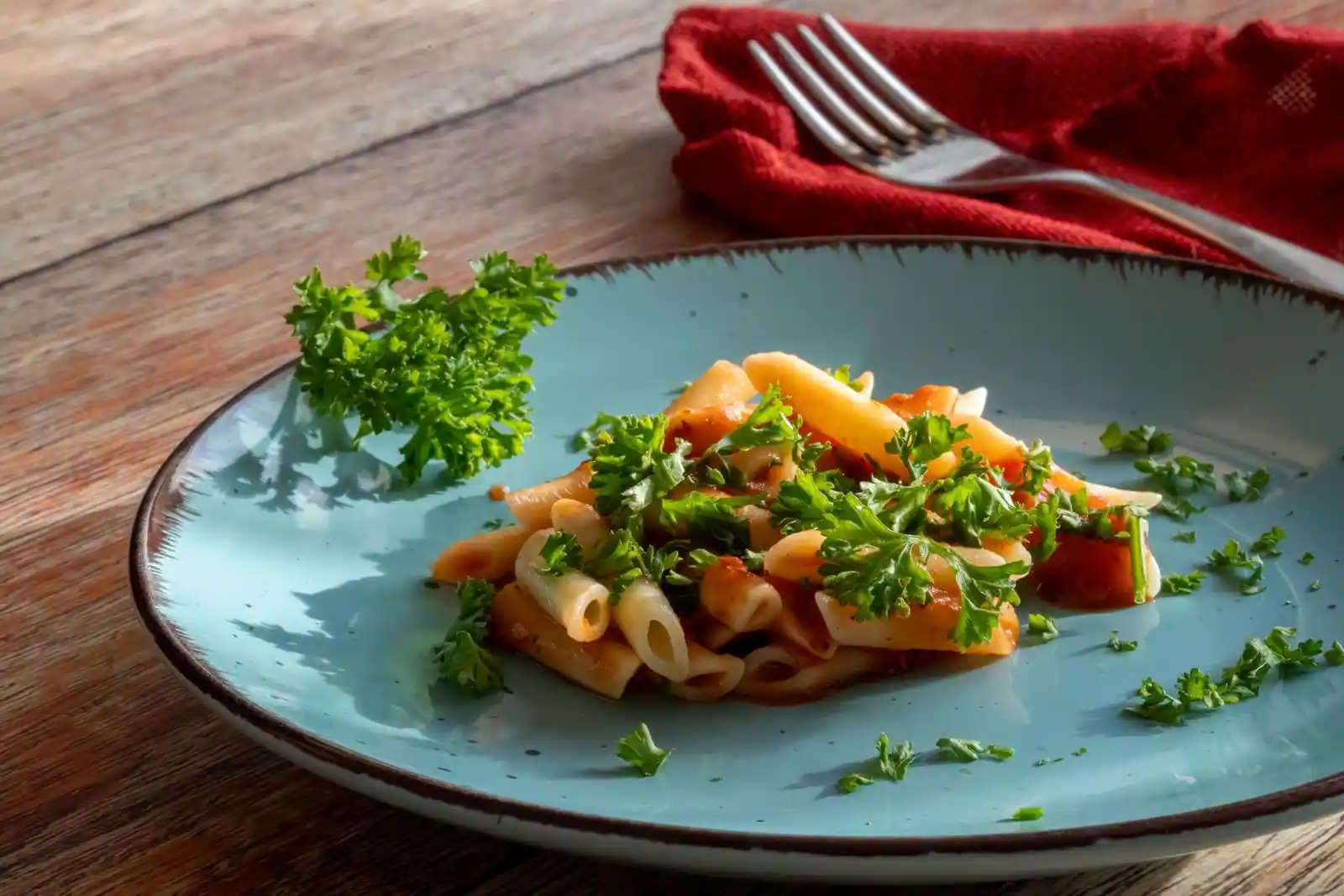 Assiette de pâtes penne à la sauce tomate parsemées de persil frais, sur une table en bois