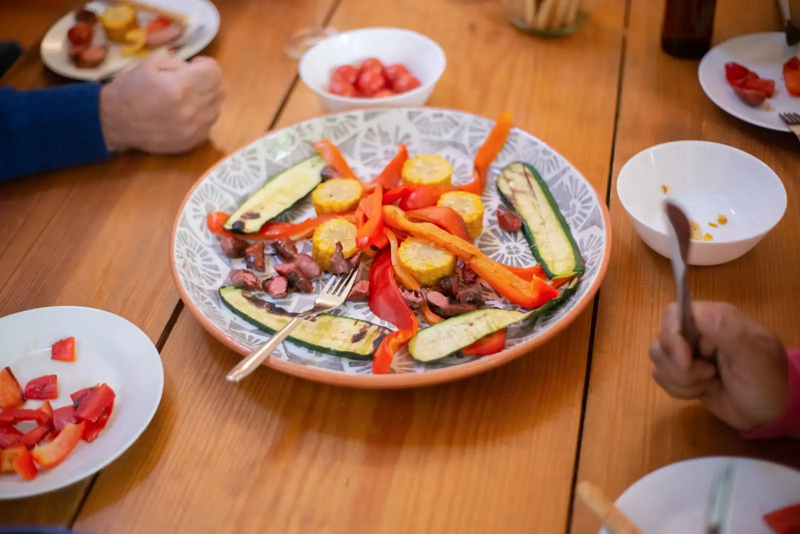 Repas convivial partagé autour d'une grande table en bois garnie de légumes grillés