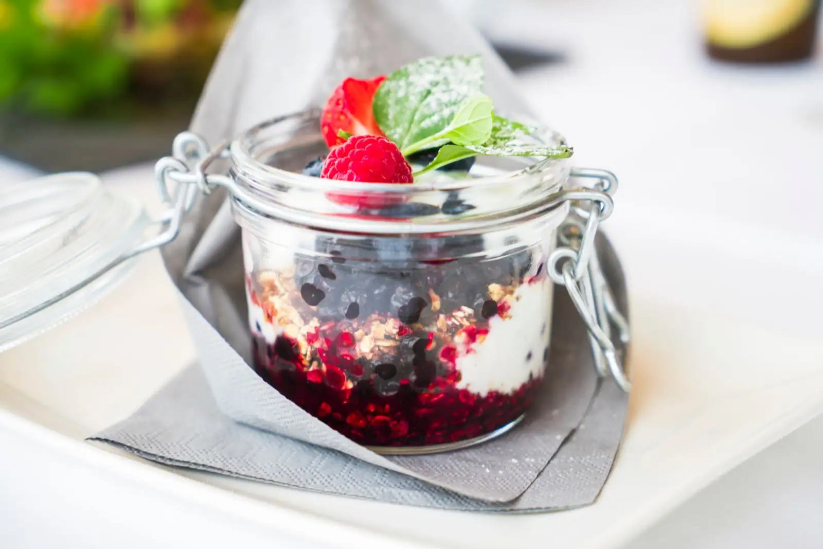 Dessert en verrine avec crème, fruits rouges et crumble, décoré d'une framboise et de menthe
