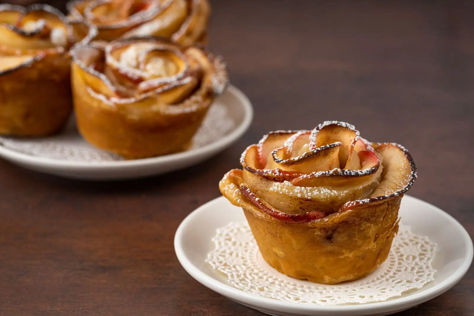 Roses de pommes en pâte feuilletée saupoudrées de sucre glace sur une assiette, dessert d'hiver