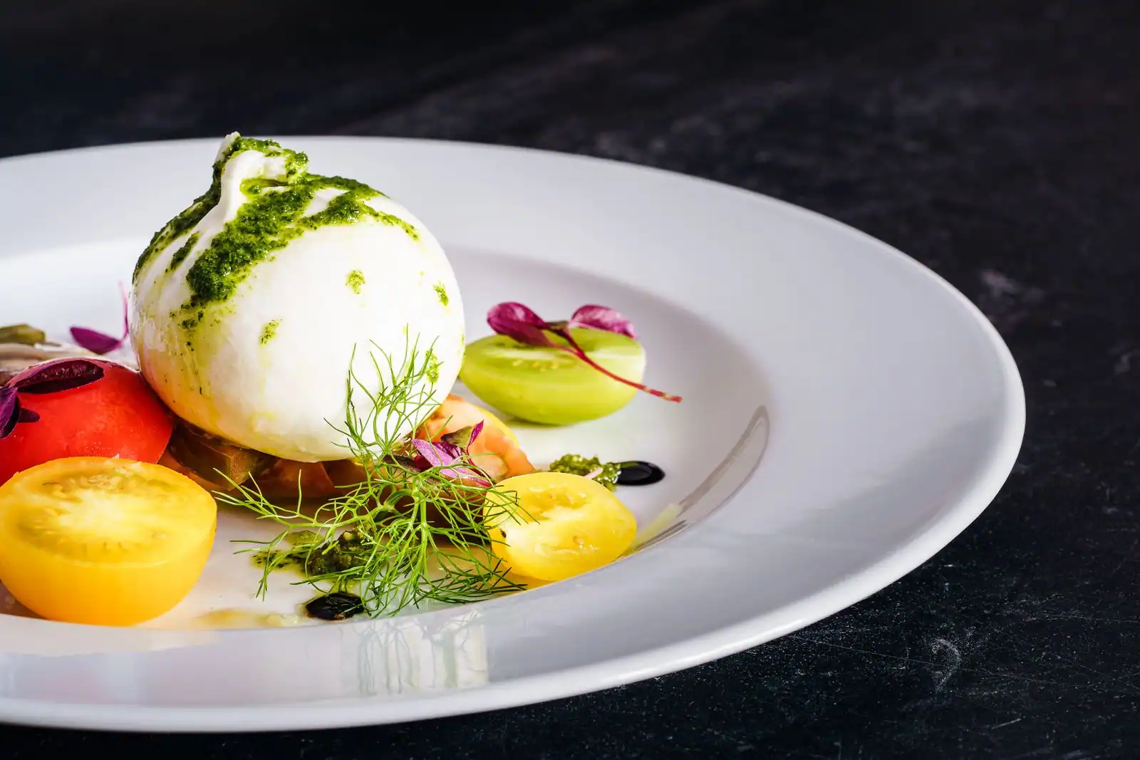Entrée dressée : boule de burrata au pesto, tomates multicolores et herbes sur assiette blanche