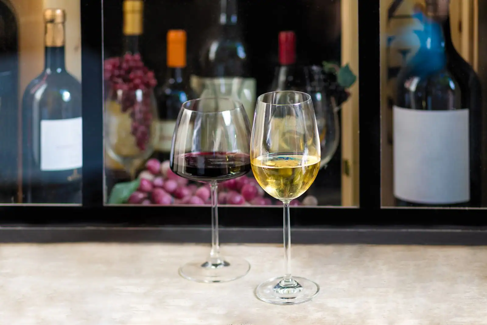 Verres de vin rouge et de vin blanc posés devant une vitrine garnie de bouteilles de vin