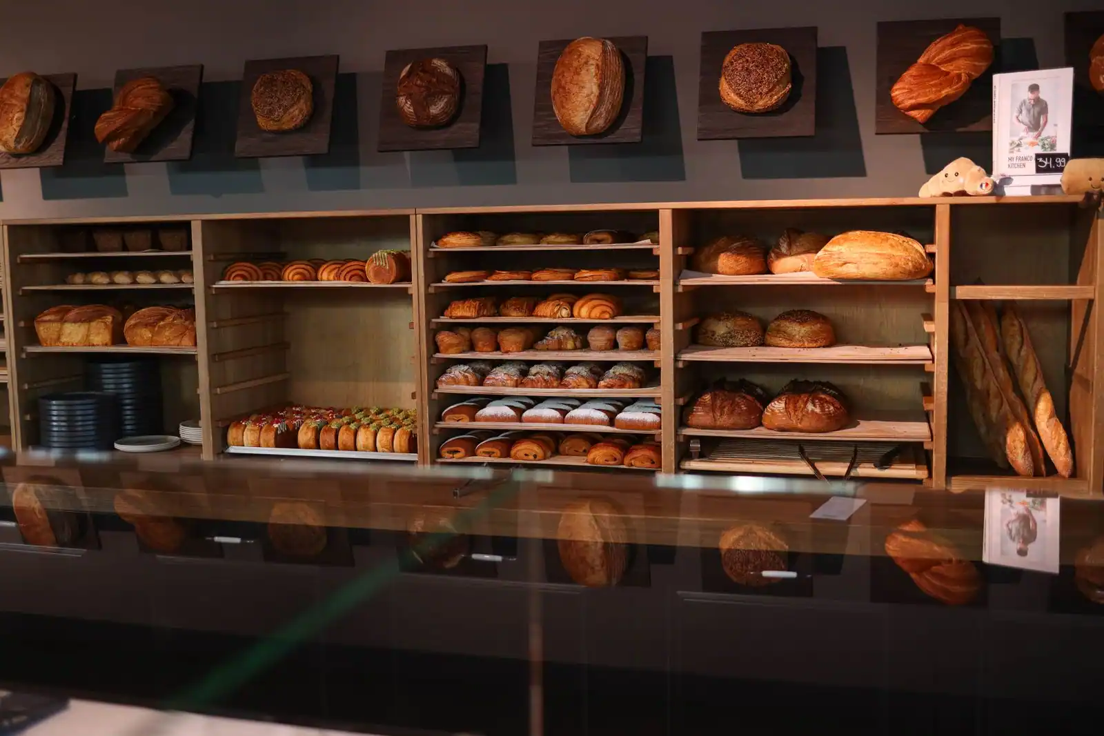 Étagères en bois d'une boulangerie garnies de pains, baguettes et viennoiseries derrière une vitre