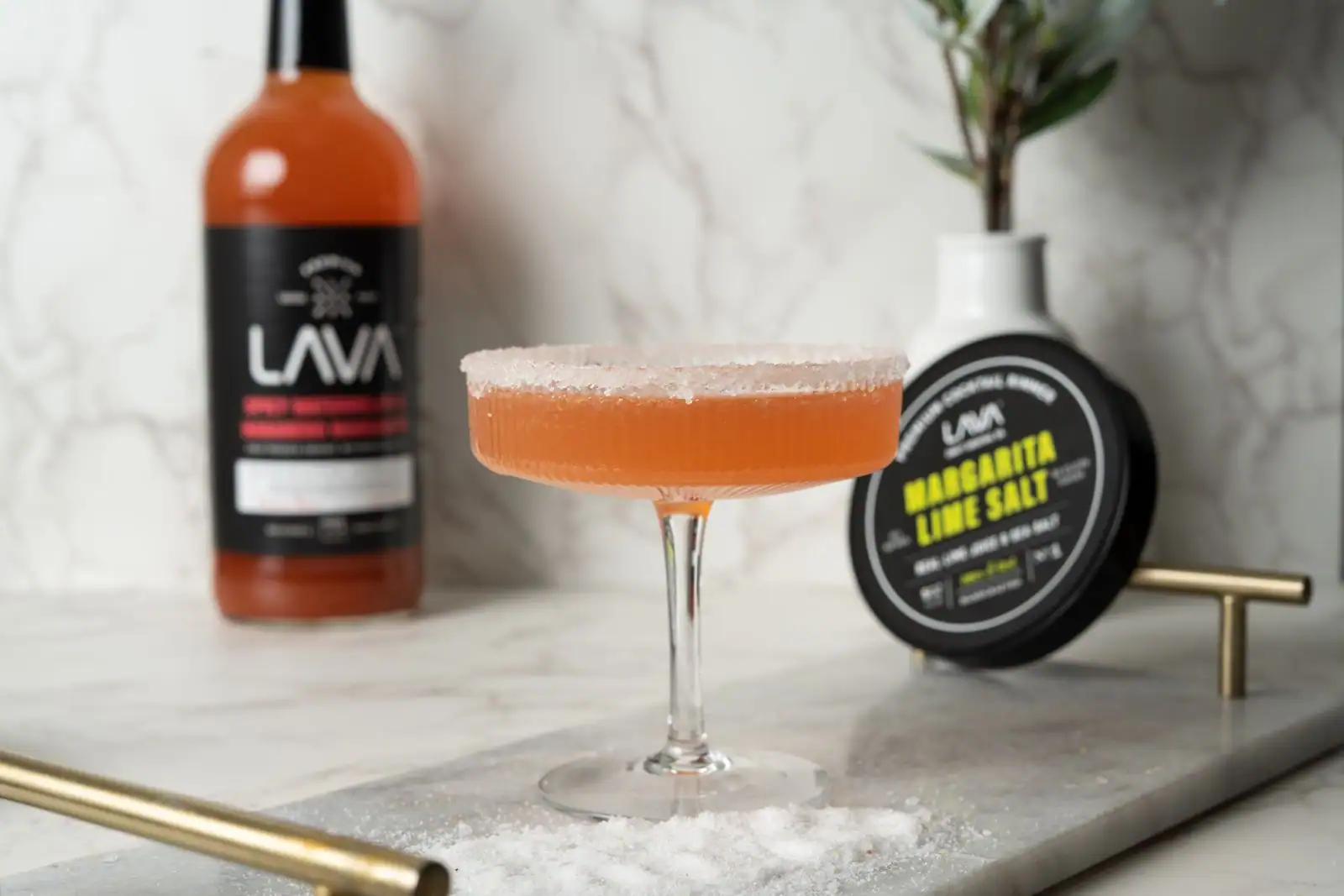 Cocktail margarita dans un verre à pied au bord givré de sel, posé sur un plateau de marbre clair