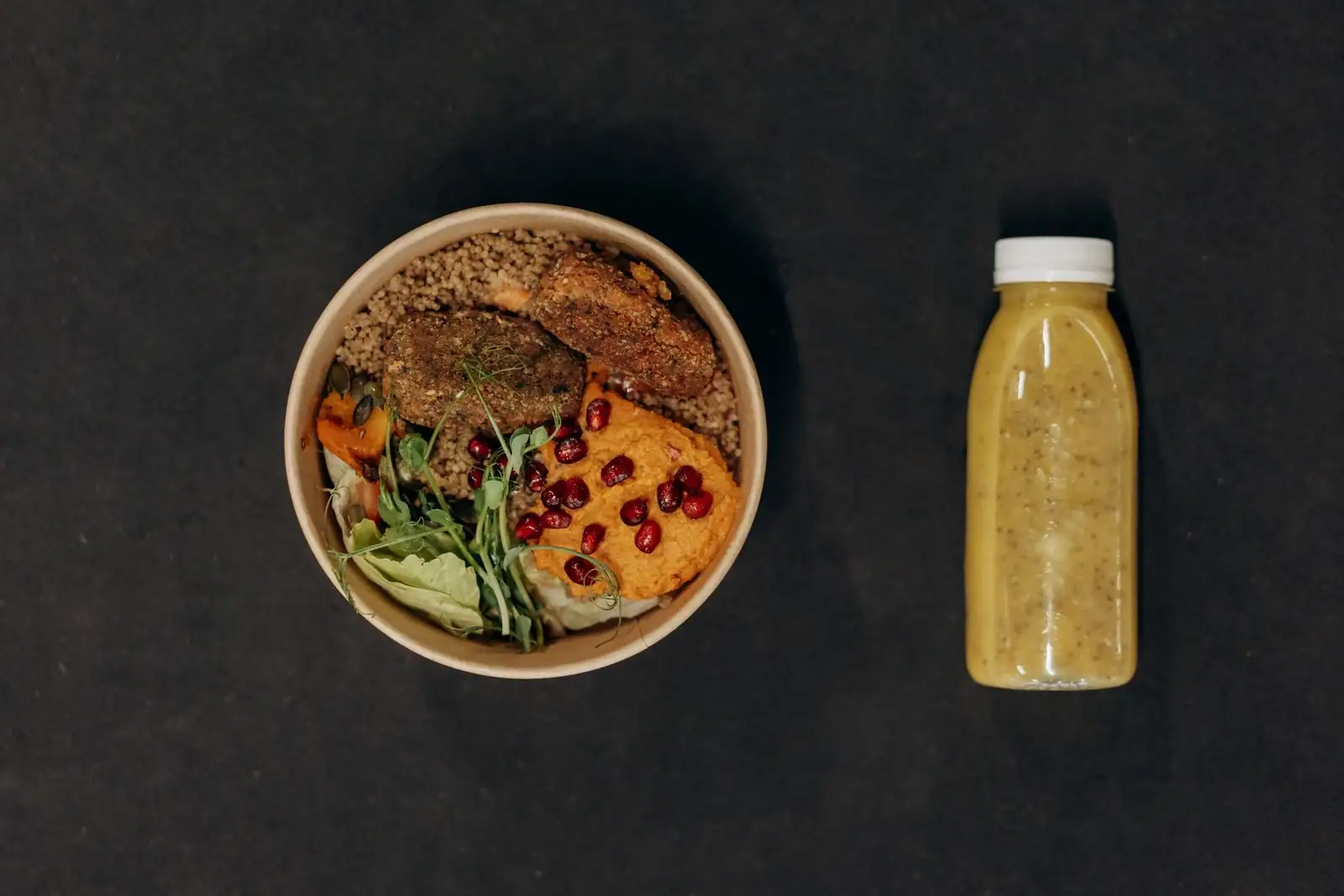 Bol de quinoa aux légumes rôtis, jeunes pousses et grains de grenade, à côté d'un jus vert