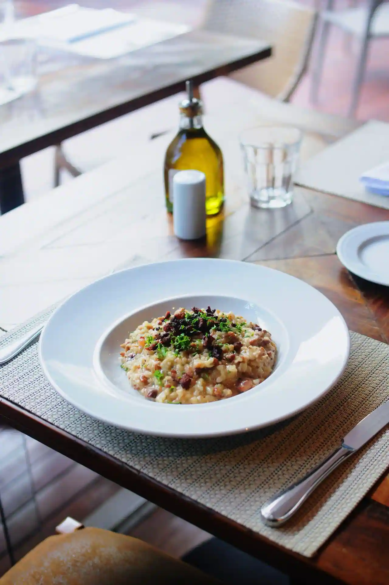 Risotto crémeux garni de petits dés de charcuterie croustillants et de persil, dans une assiette creuse