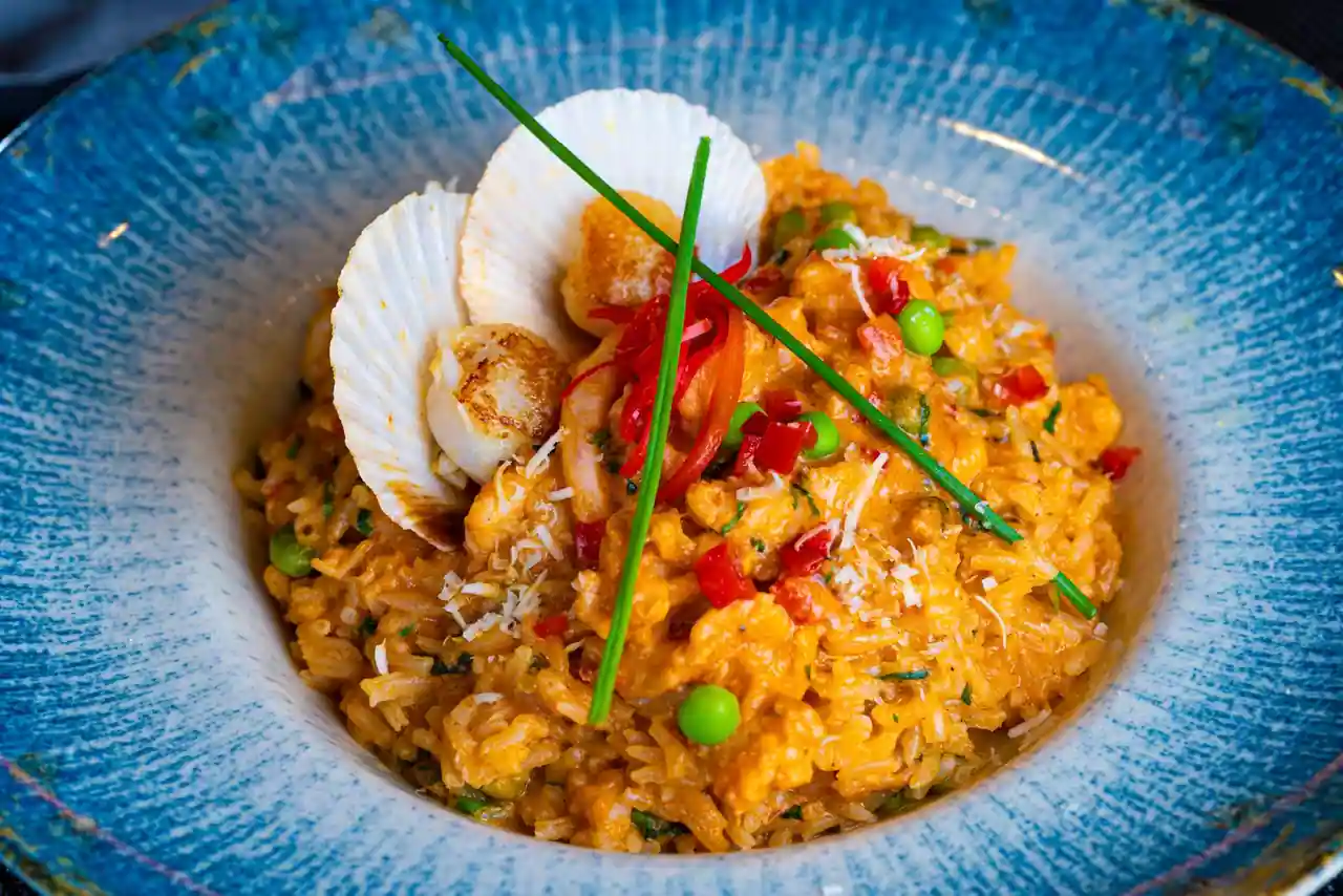 Risotto aux noix de Saint-Jacques servi dans un bol, garni d'une Saint-Jacques poêlée dans sa coquille et de ciboulette.