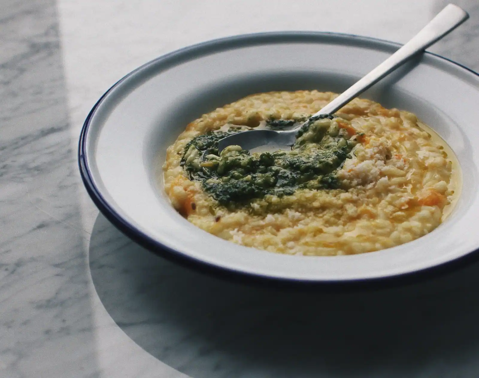 Assiette creuse de risotto crémeux nappé d'un filet de pesto, cuillère posée dans le plat