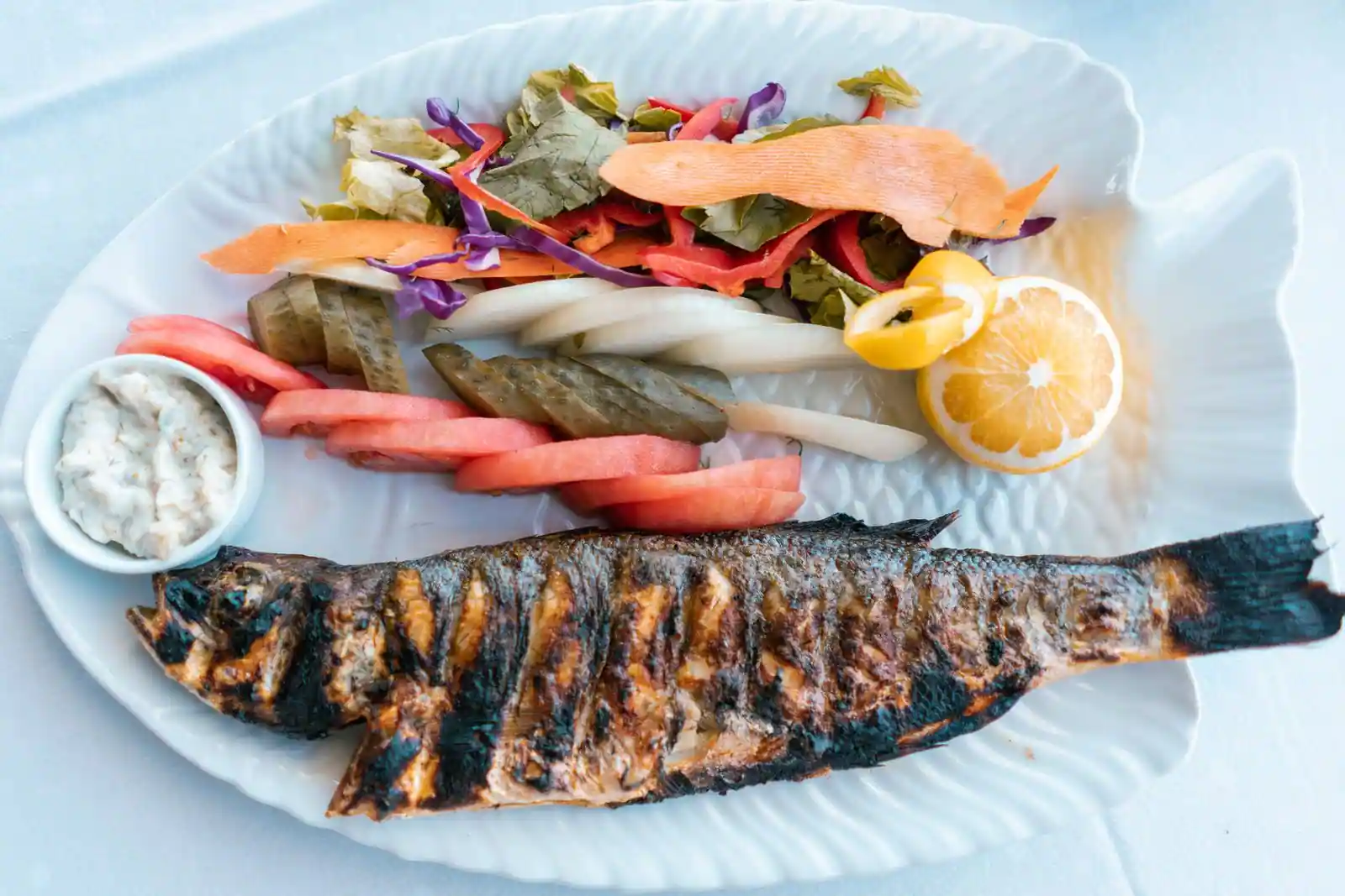 Poisson grillé servi avec des légumes et du citron dans une assiette