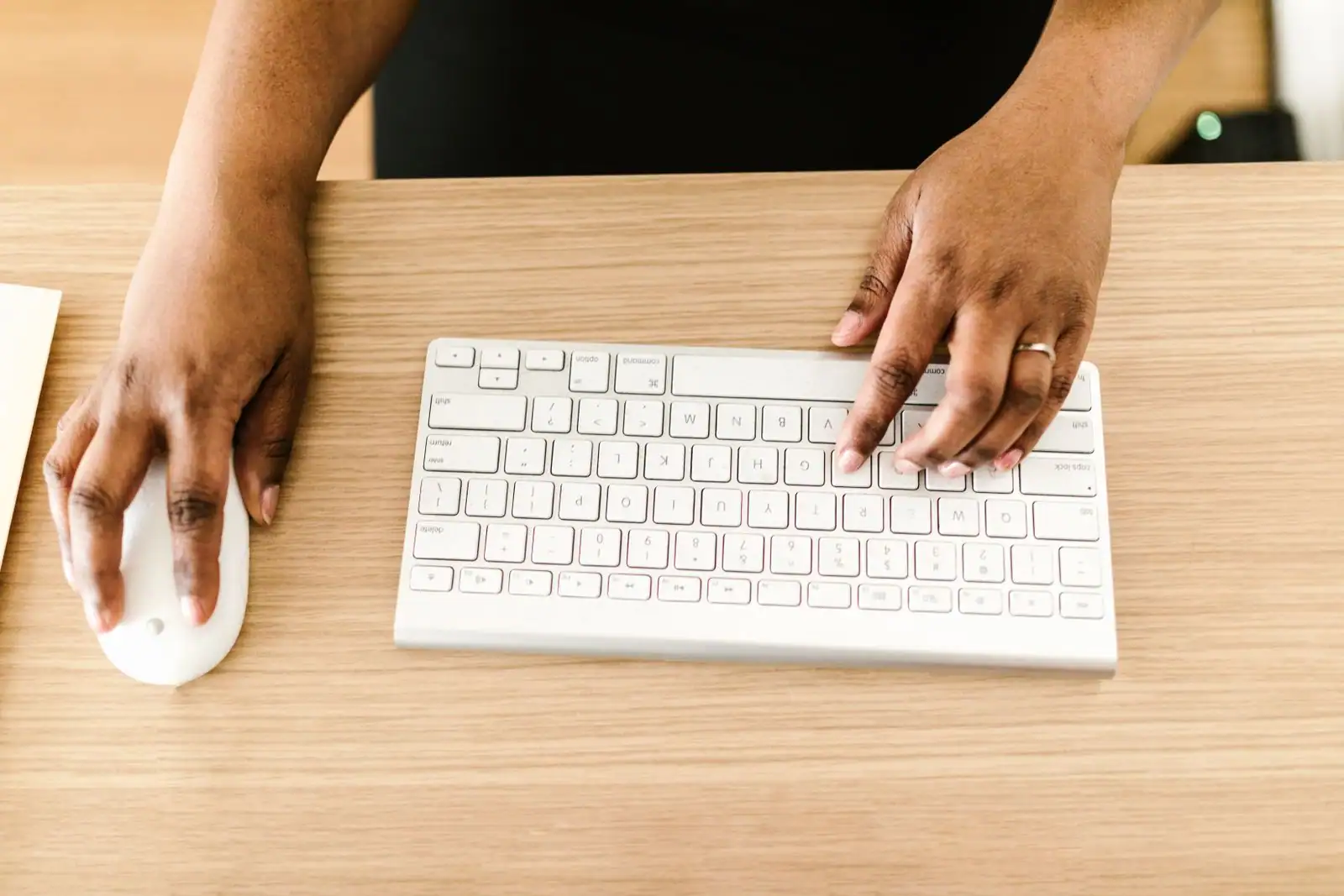 Vue de dessus des mains d'une personne sur un clavier blanc sans fil, l'autre main posée sur une souris