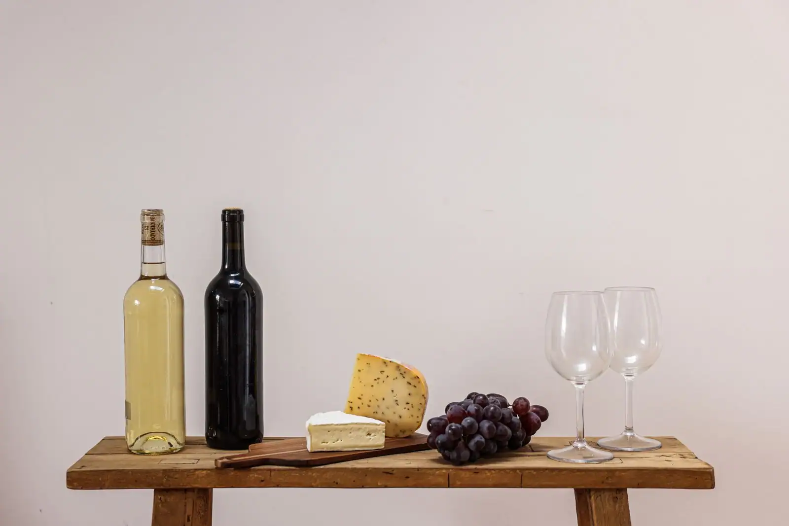 Bouteilles de vin blanc et rouge, fromages, grappe de raisin et deux verres sur une table en bois