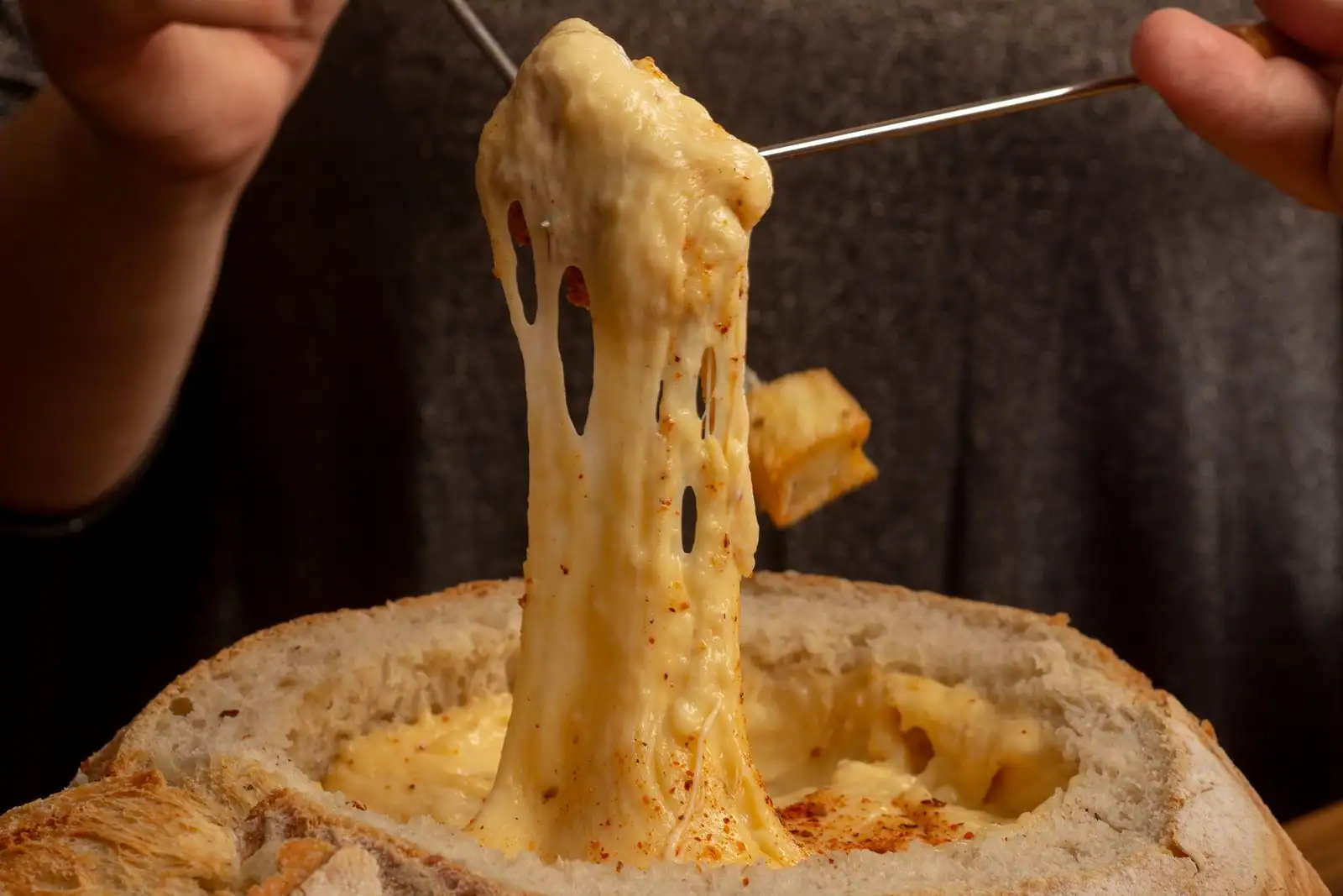 Fondue au fromage fondu servie dans un pain, une fourchette soulève un fil de fromage étiré