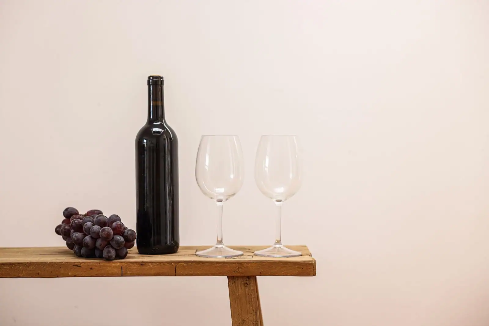 Bouteille de vin rouge, grappe de raisin et deux verres vides sur une table en bois rustique