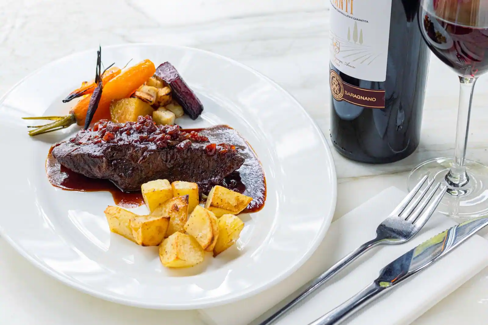 Bœuf braisé au vin rouge servi avec légumes et pommes de terre, et un verre de vin rouge