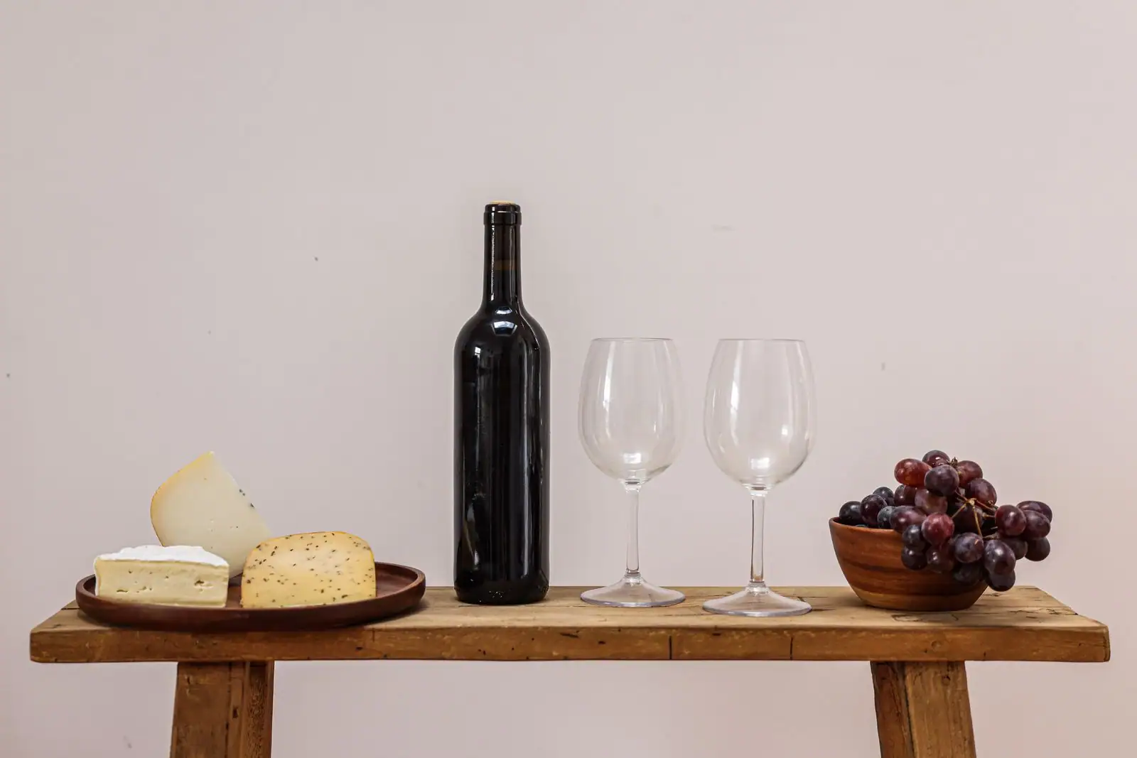 Bouteille de vin, deux verres, plateau de fromages et grappe de raisin sur une table en bois