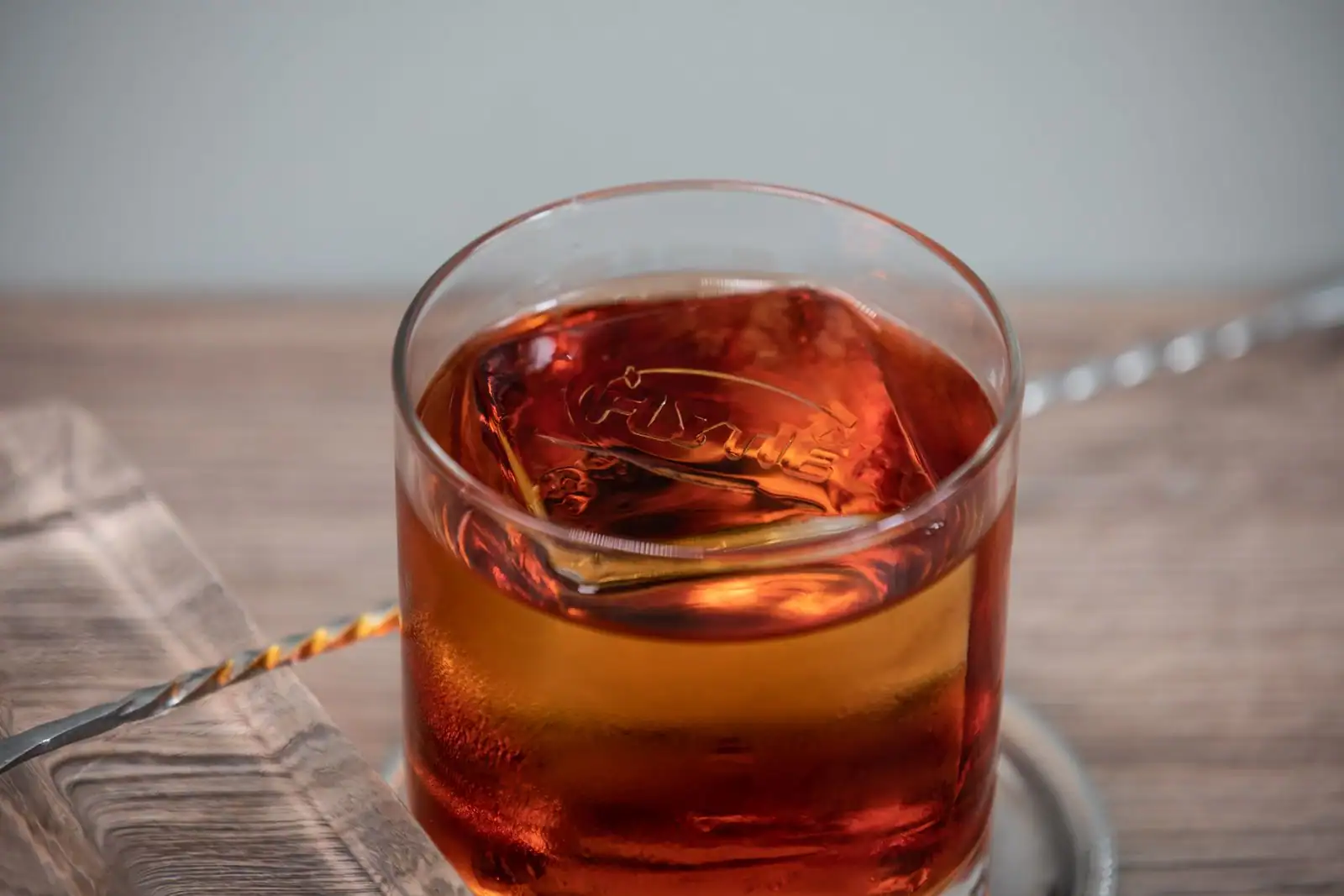 Verre de whisky ambré avec un gros glaçon dans un tumbler, posé sur un comptoir en bois