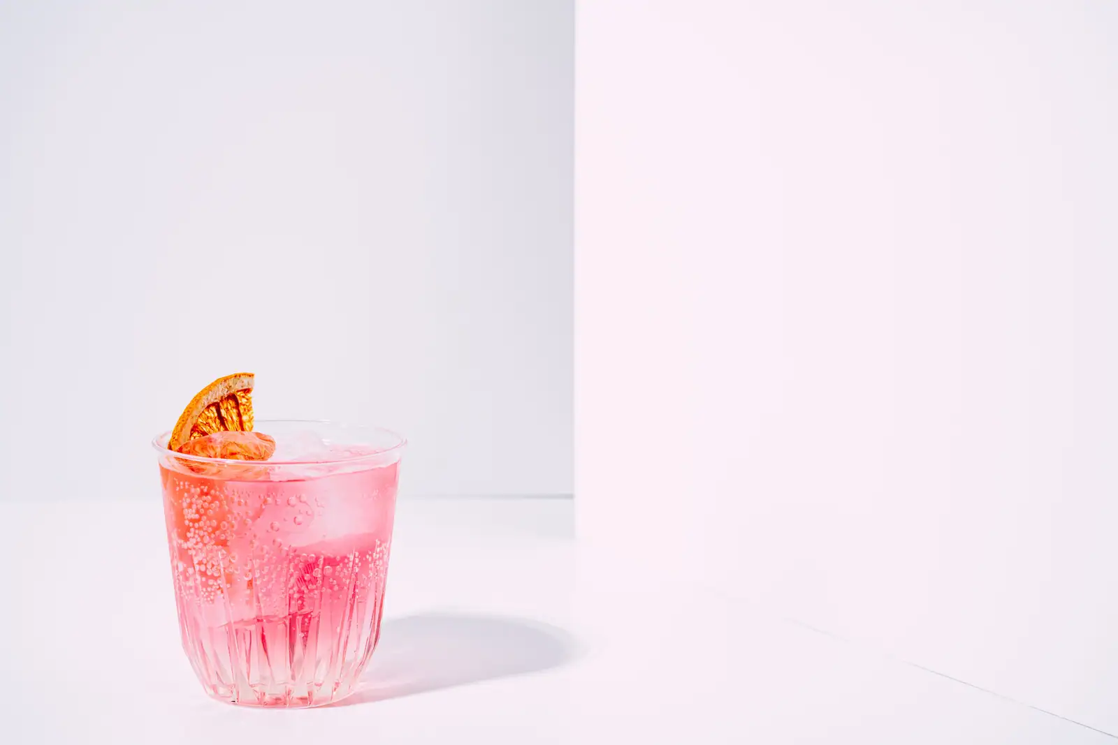 Cocktail rosé pétillant servi sur glace, garni d'une rondelle d'agrume séchée, sur fond clair