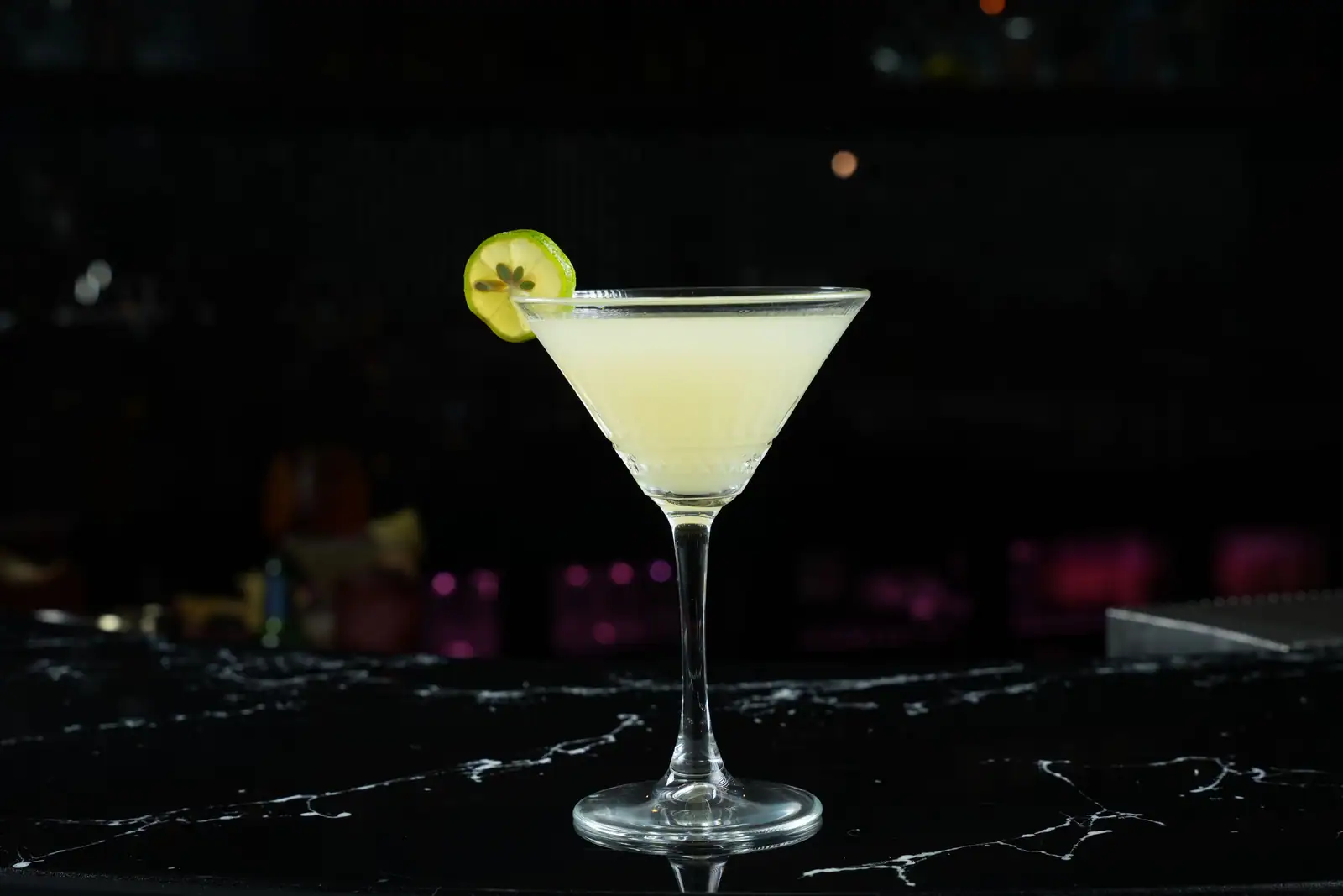 Cocktail clair servi dans un verre à pied, garni d'une rondelle de citron vert, sur un comptoir de bar